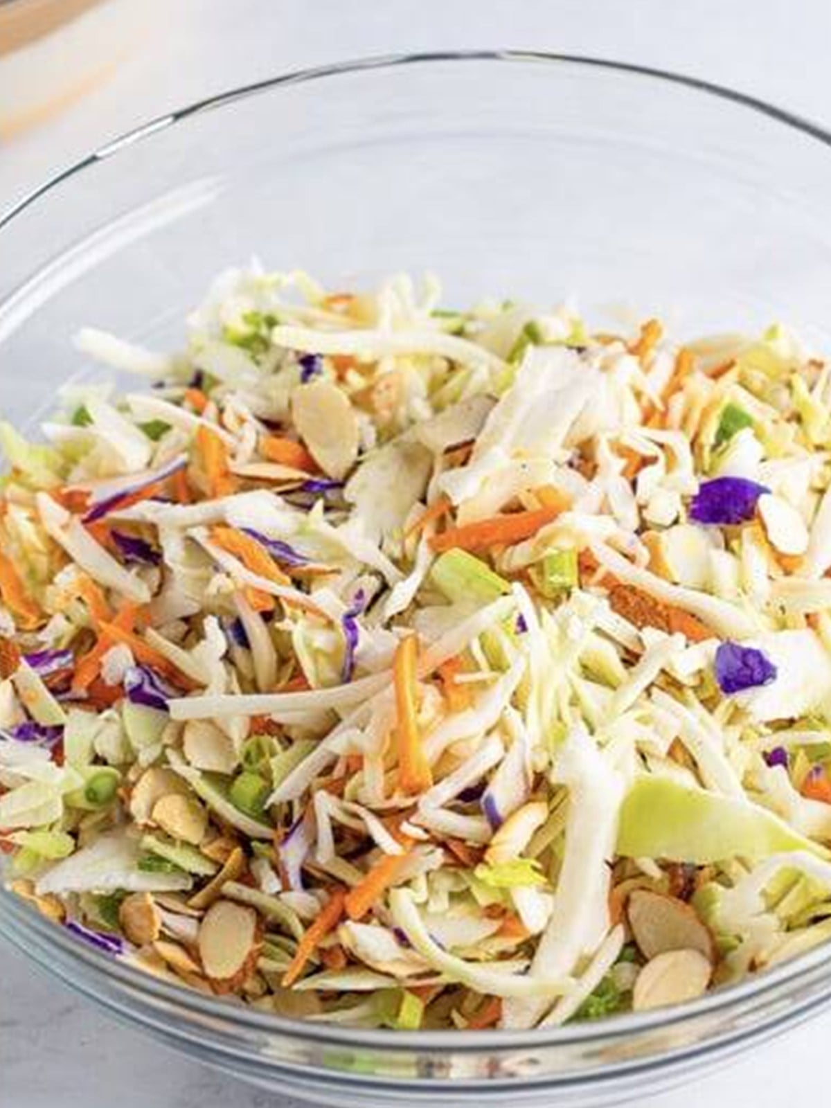 Slaw mix tossed with scallions and almonds in a bowl.