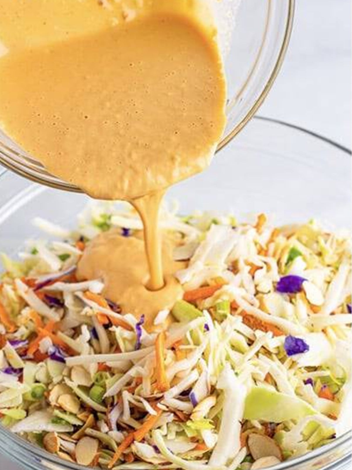 Pouring creamy dressing over the Asian slaw.