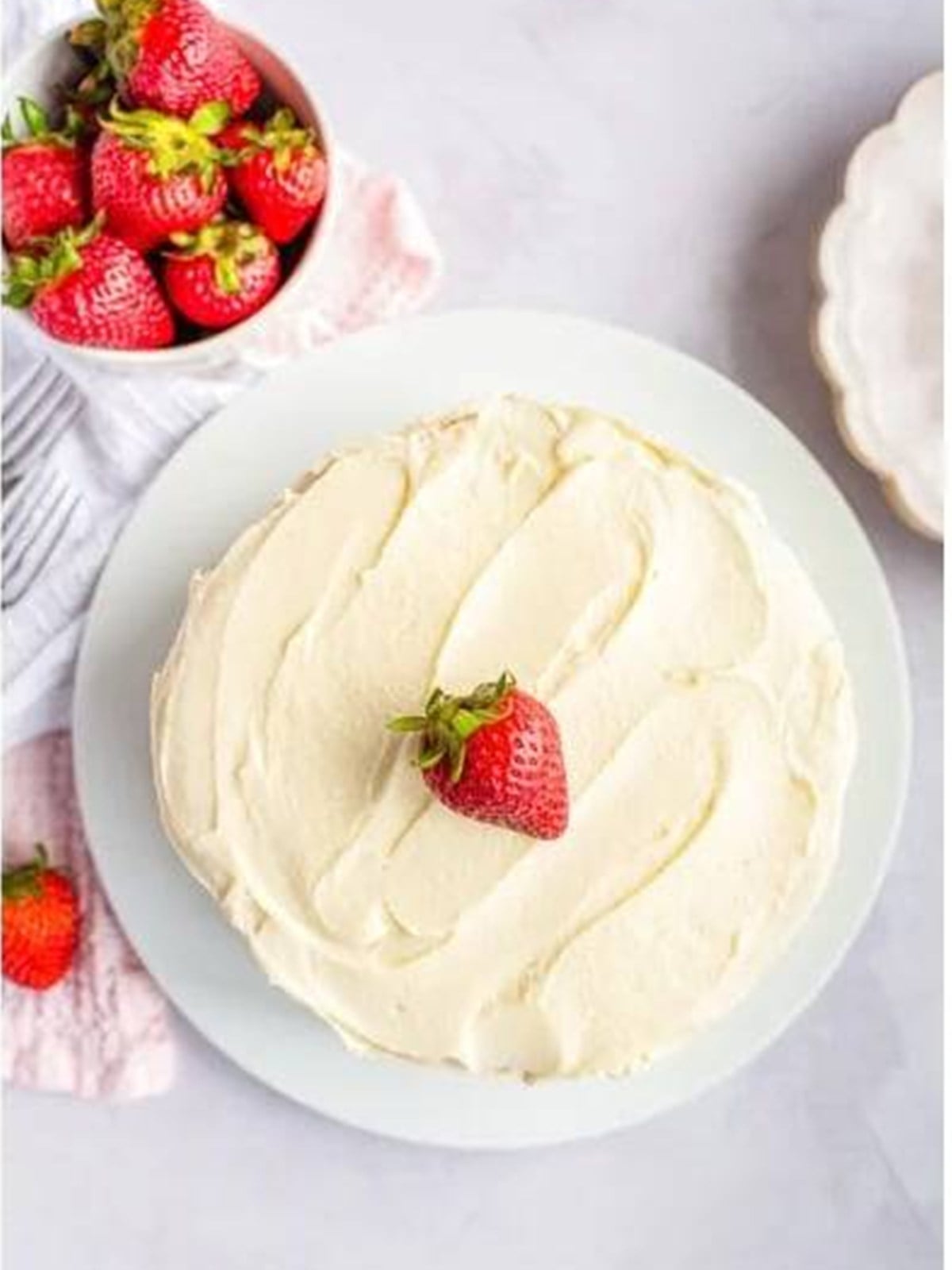 Finished frosted strawberry shortcake cheesecake cake topped with a strawberry.