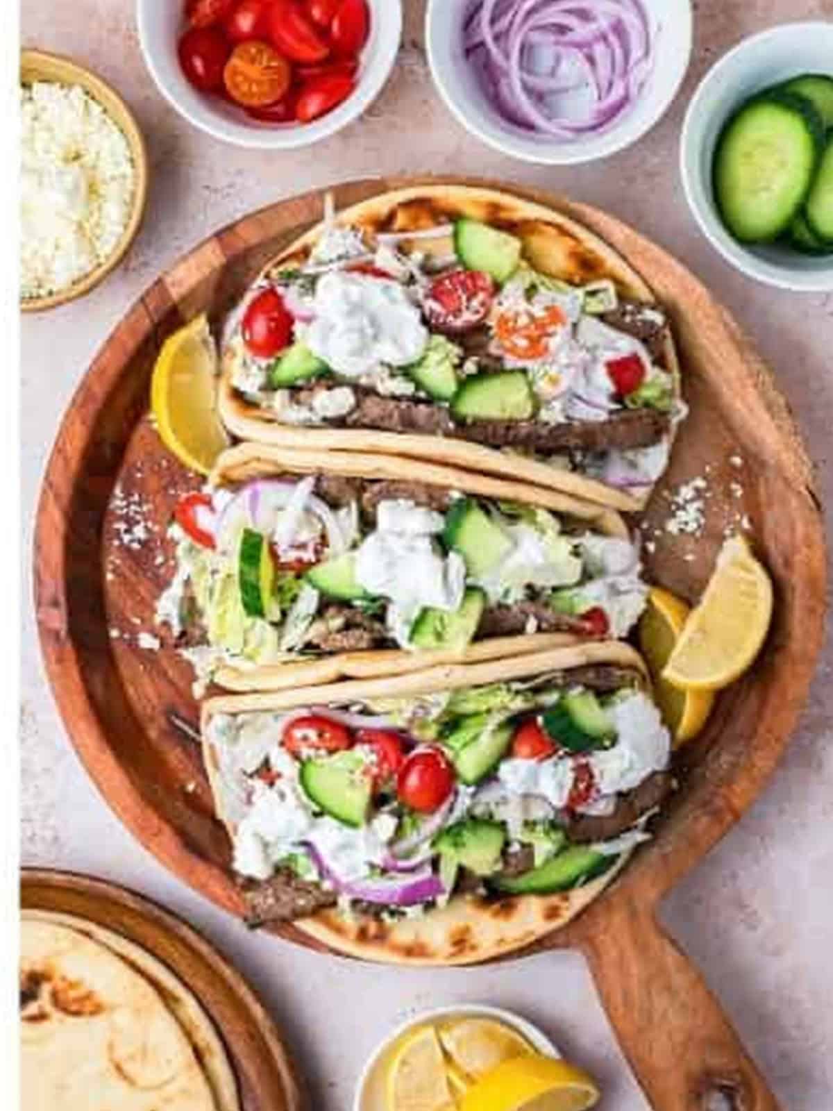Assembled Greek gyros on pita topped with tzatziki, tomatoes, and cucumber
