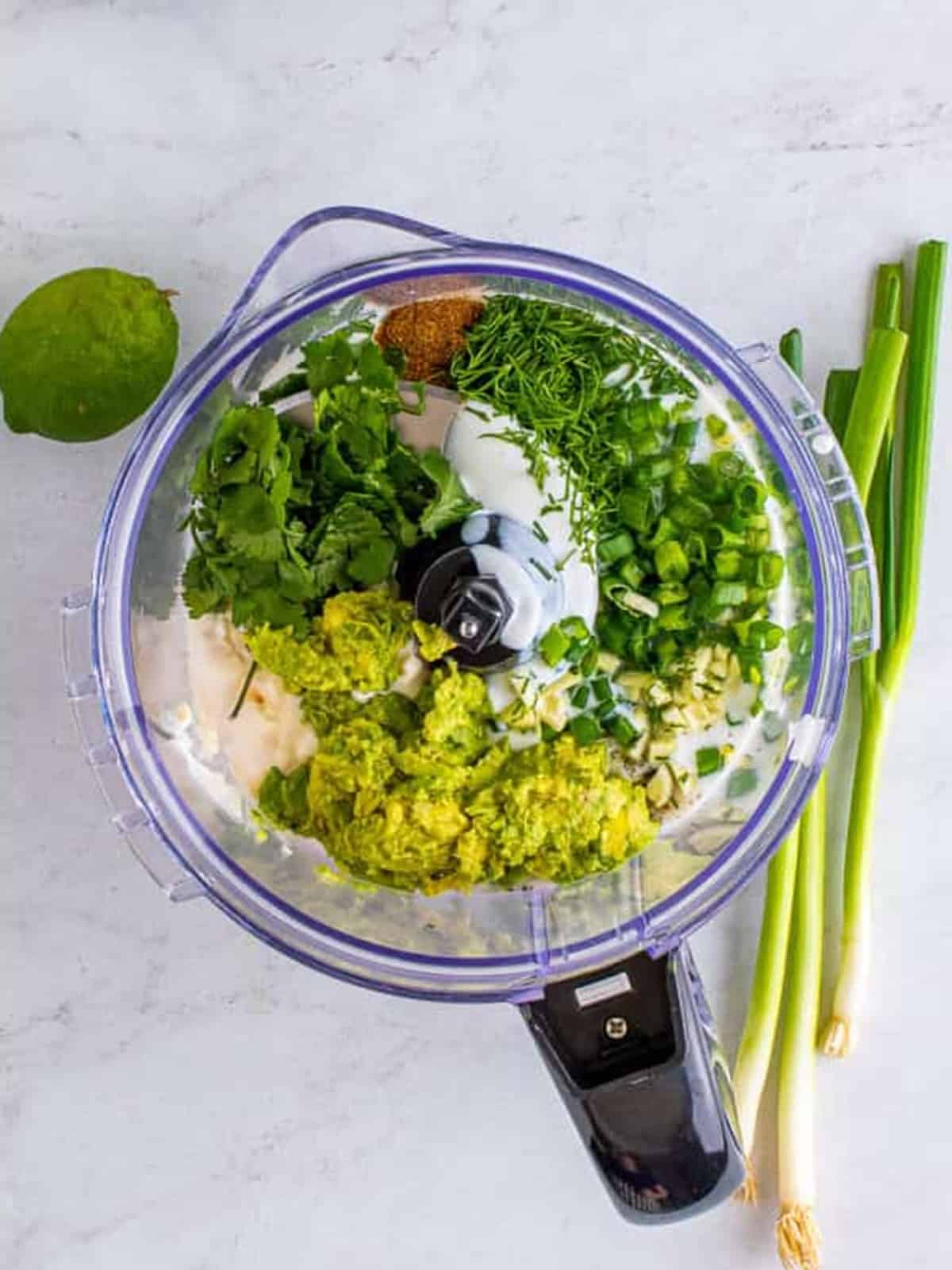 Avocado, buttermilk, mayonnaise, cilantro, scallions, and seasonings added to a food processor for avocado ranch.