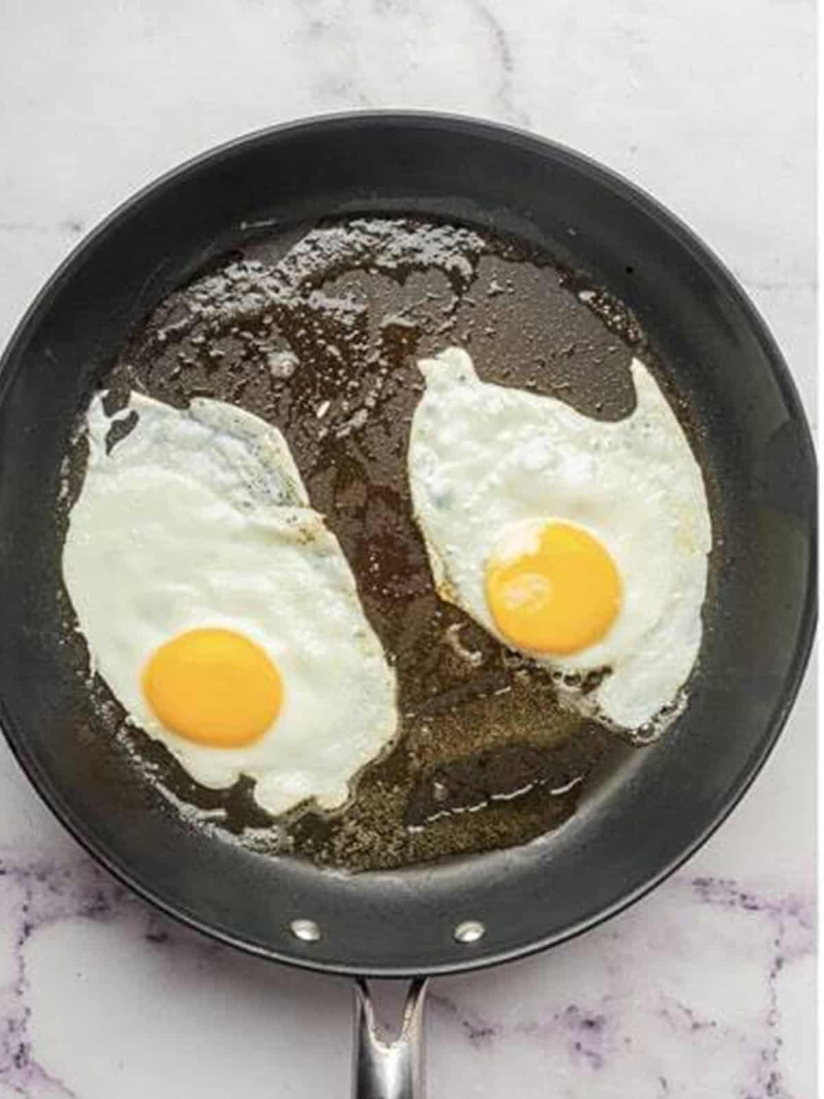 Two eggs frying in olive oil in a skillet for avocado toast.