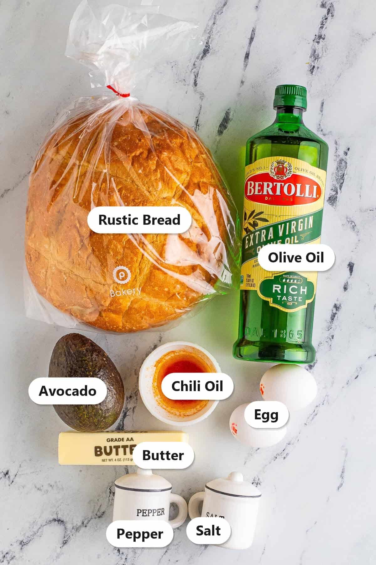 Labeled ingredients for avocado toast including rustic bread, avocado, olive oil, butter, eggs, chili oil, salt, and pepper.