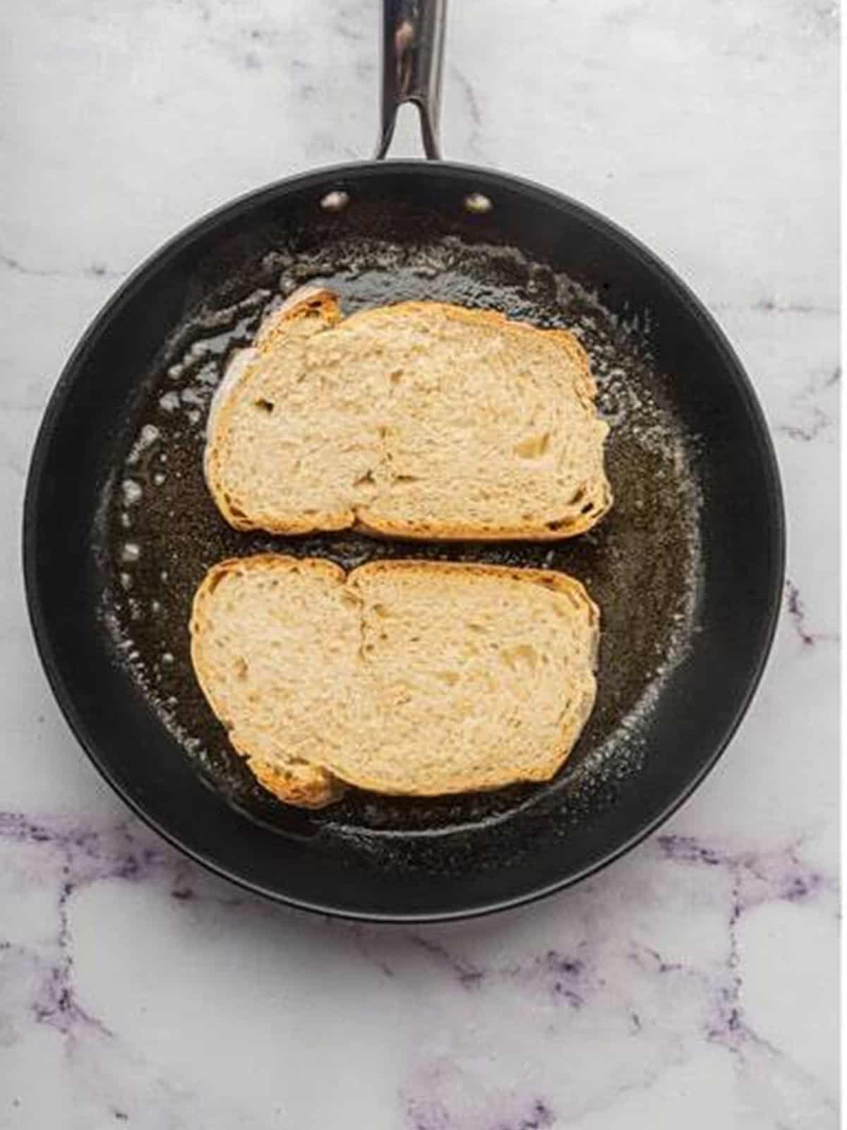 Slices of rustic bread toasting in butter in a skillet for avocado toast.