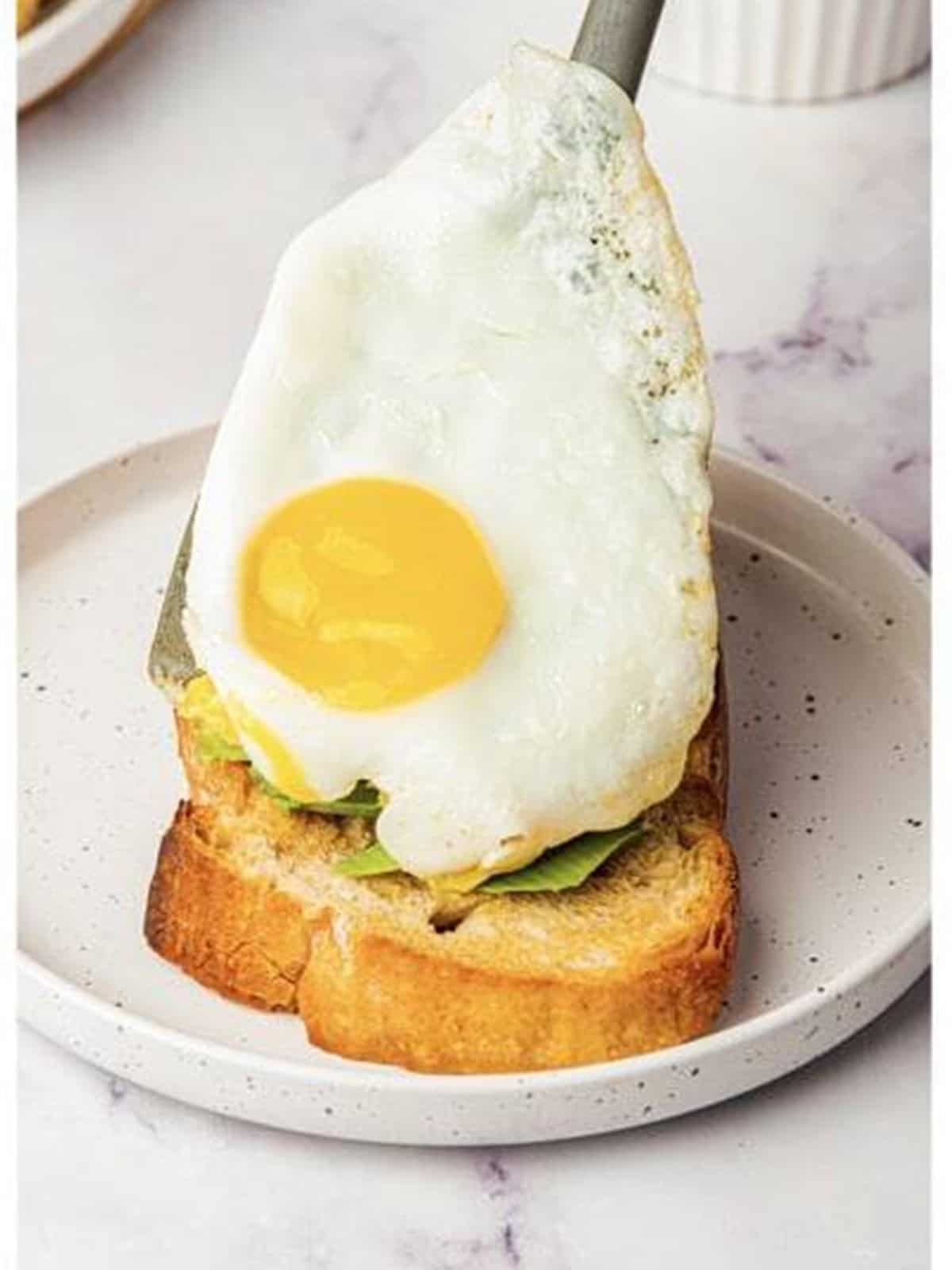 A fried egg placed on top of avocado toast.