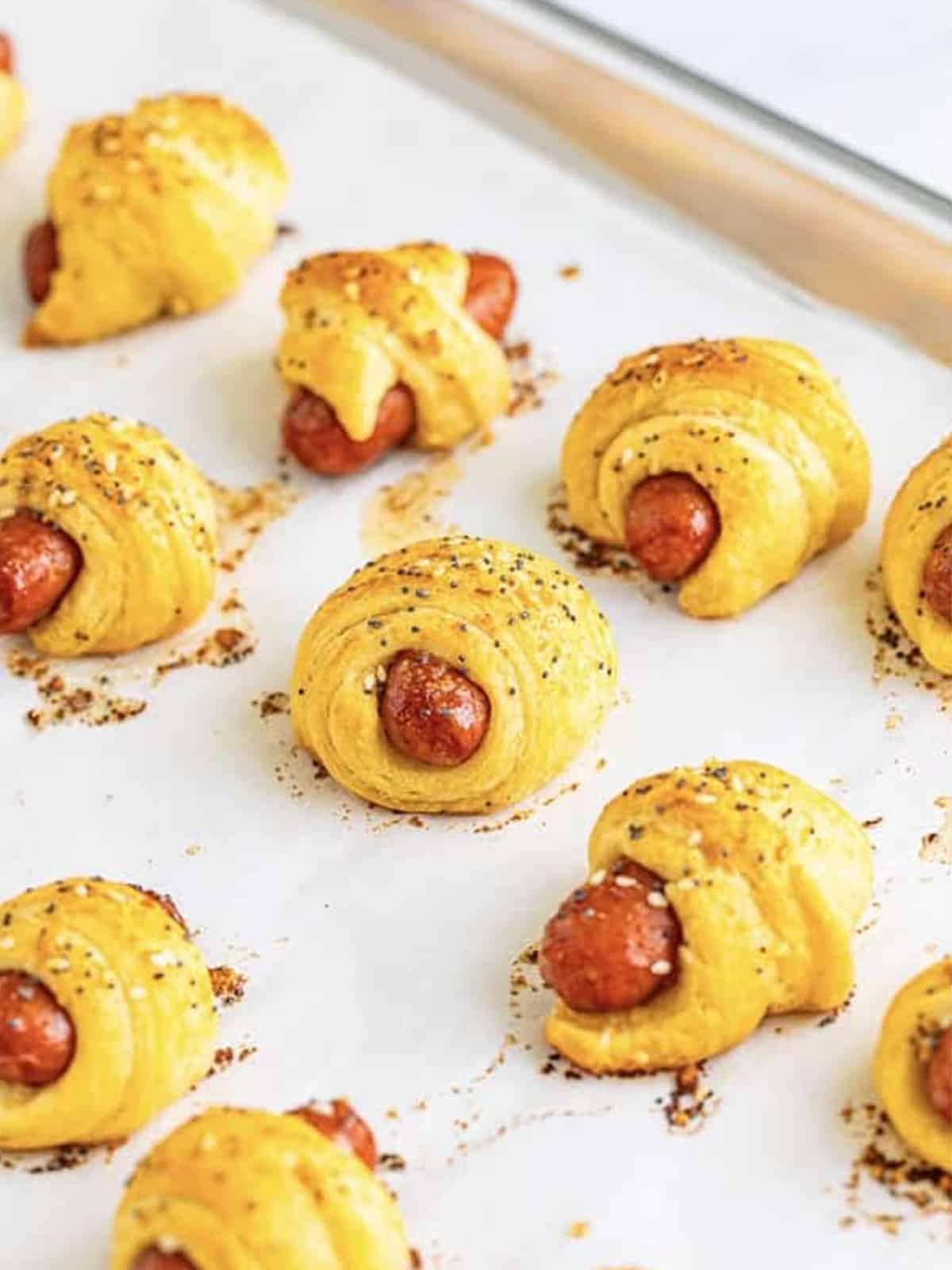 Golden baked mini pigs in a blanket topped with poppy and sesame seeds.