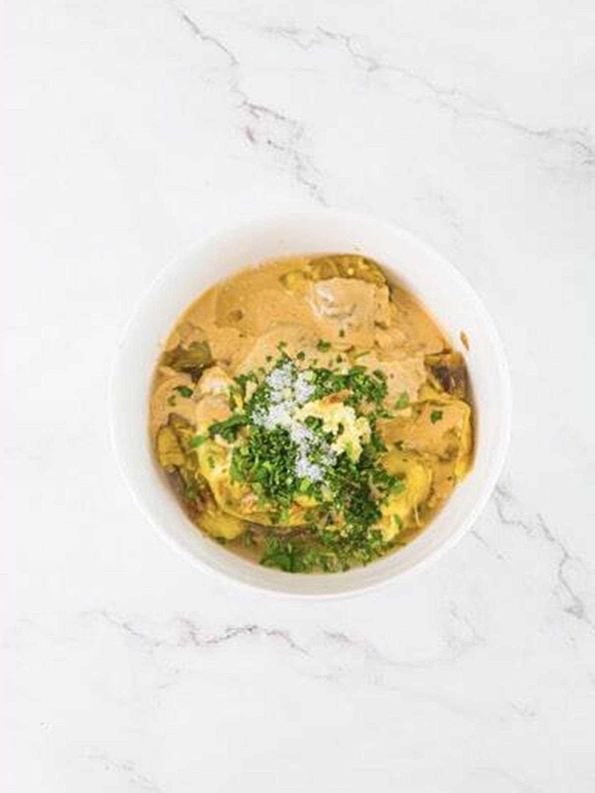 Tahini, garlic, lemon juice, and parsley added to the eggplant in a bowl.