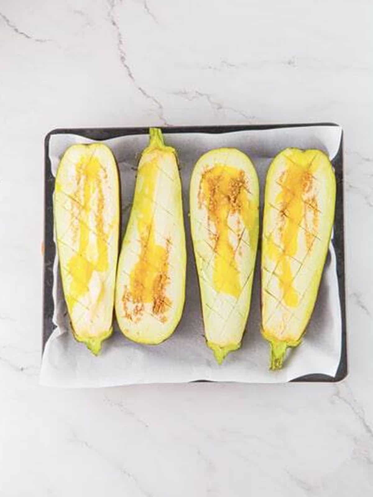 Halved eggplants brushed with olive oil on a lined baking sheet for baba ganoush.