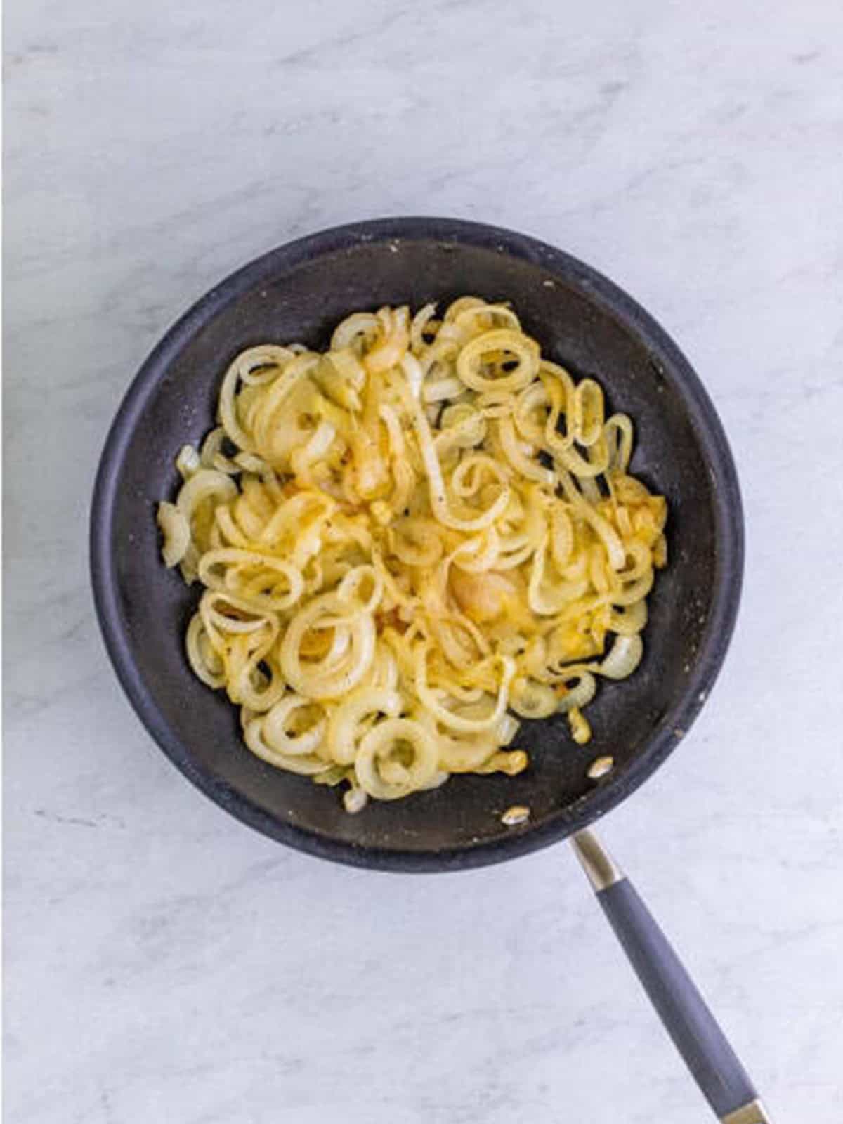 Sliced sweet onions softening in a skillet with oil.