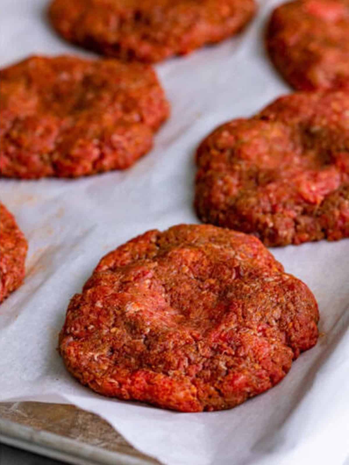 Seasoned beef formed into burger patties on a tray.