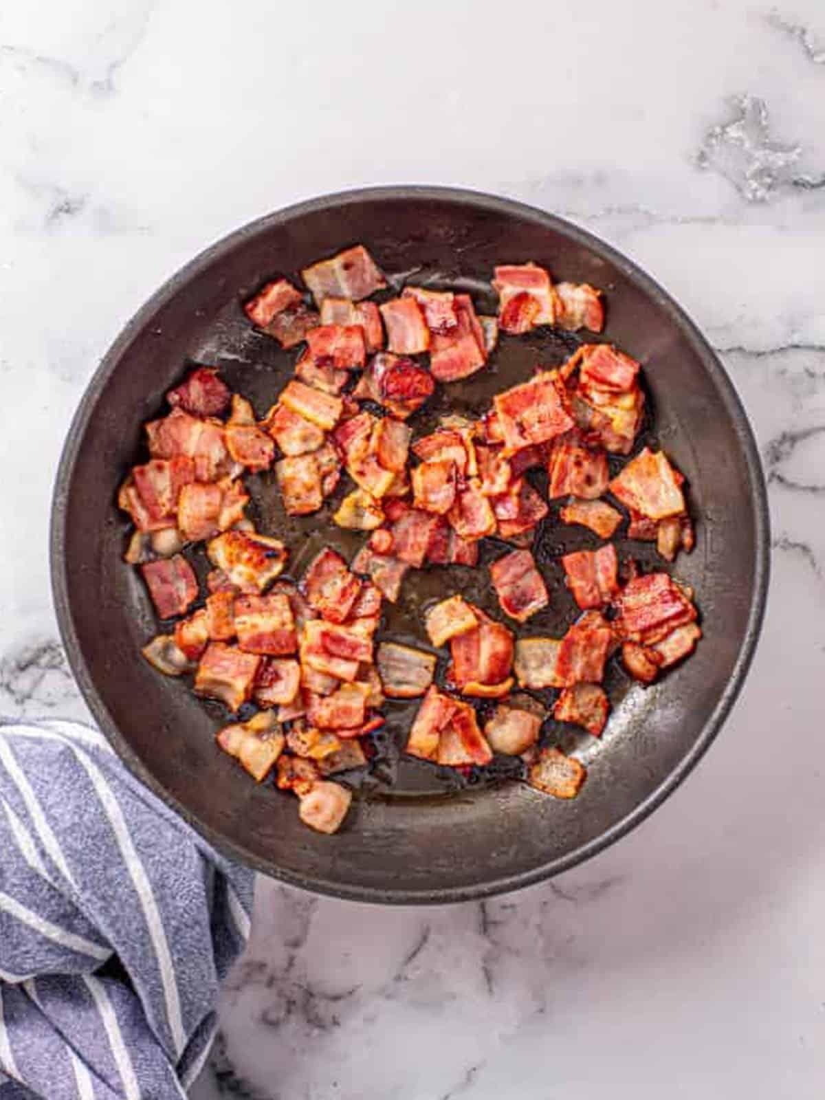Chopped thick-cut bacon fried crispy in a skillet for bacon pesto pasta.