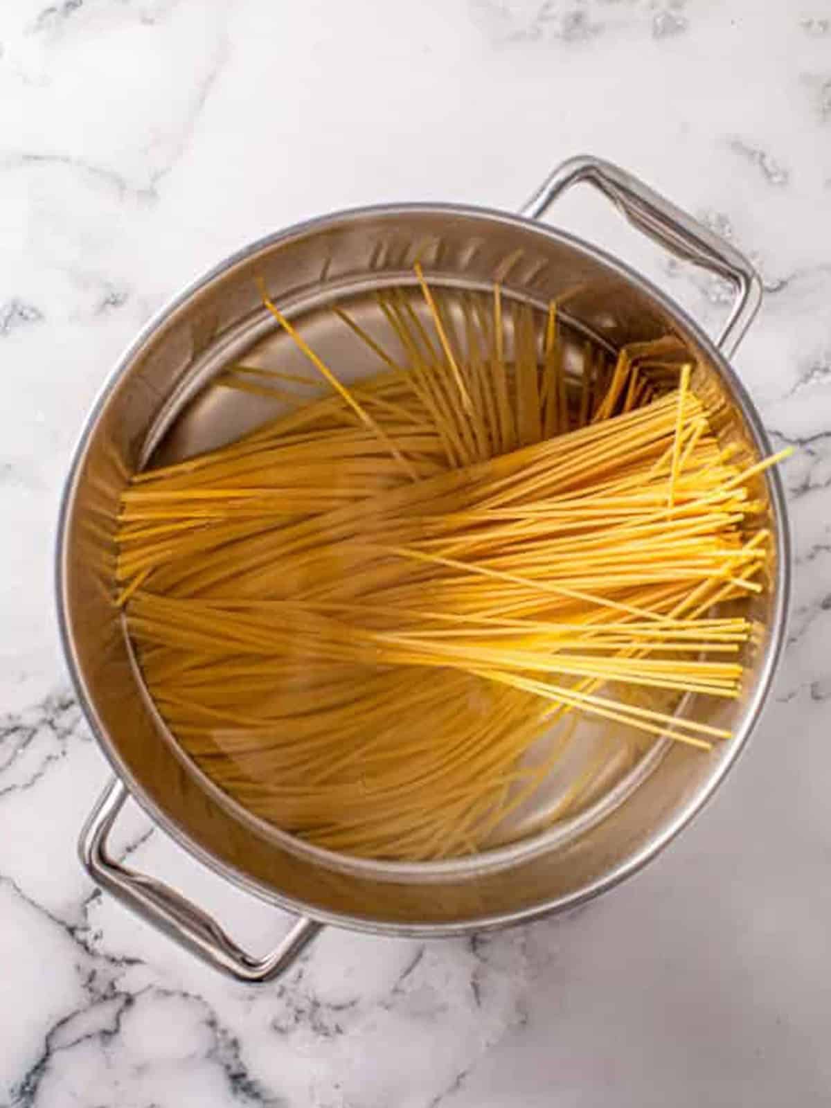 Spaghetti noodles cooking in a pot of water for bacon pesto pasta.