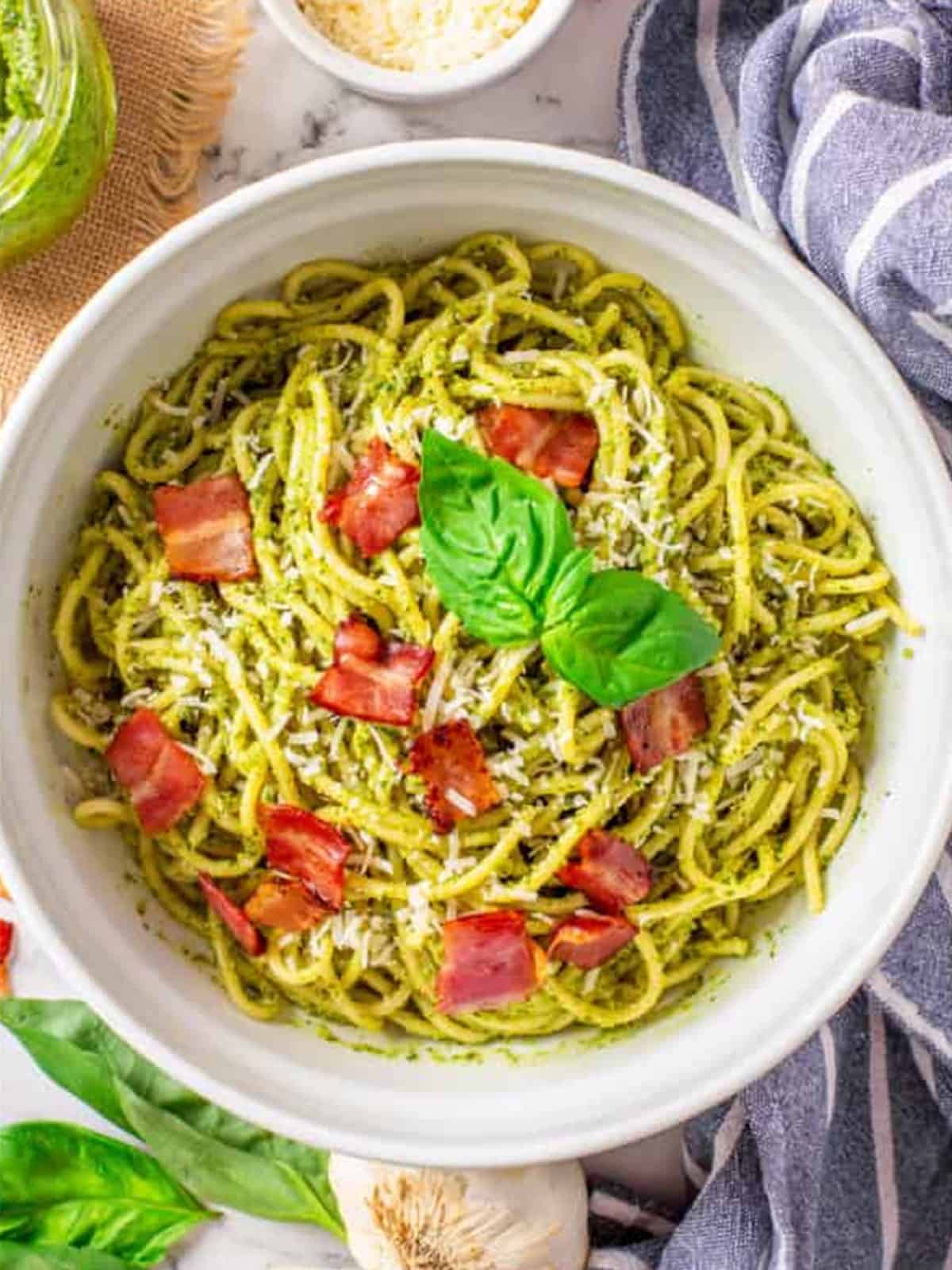 Spaghetti tossed with basil pesto and topped with crispy bacon in a white bowl.
