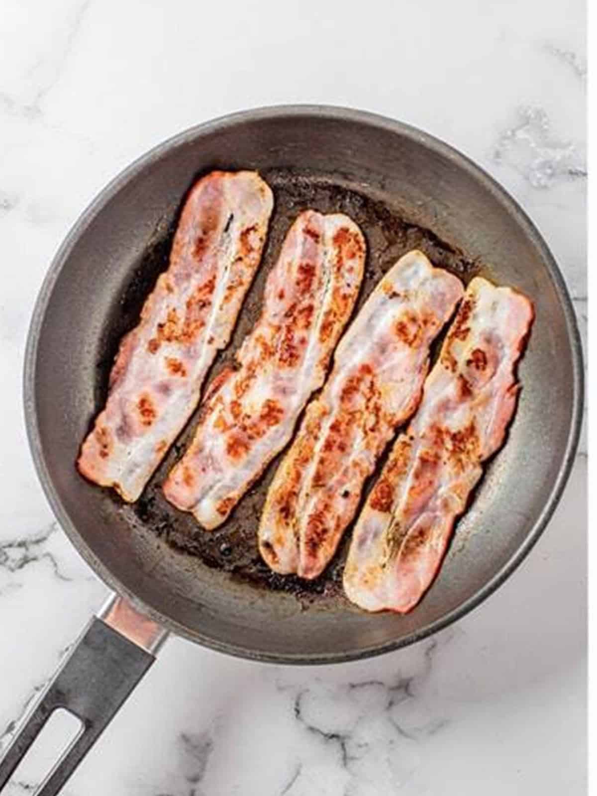 Bacon frying until crispy in a skillet.