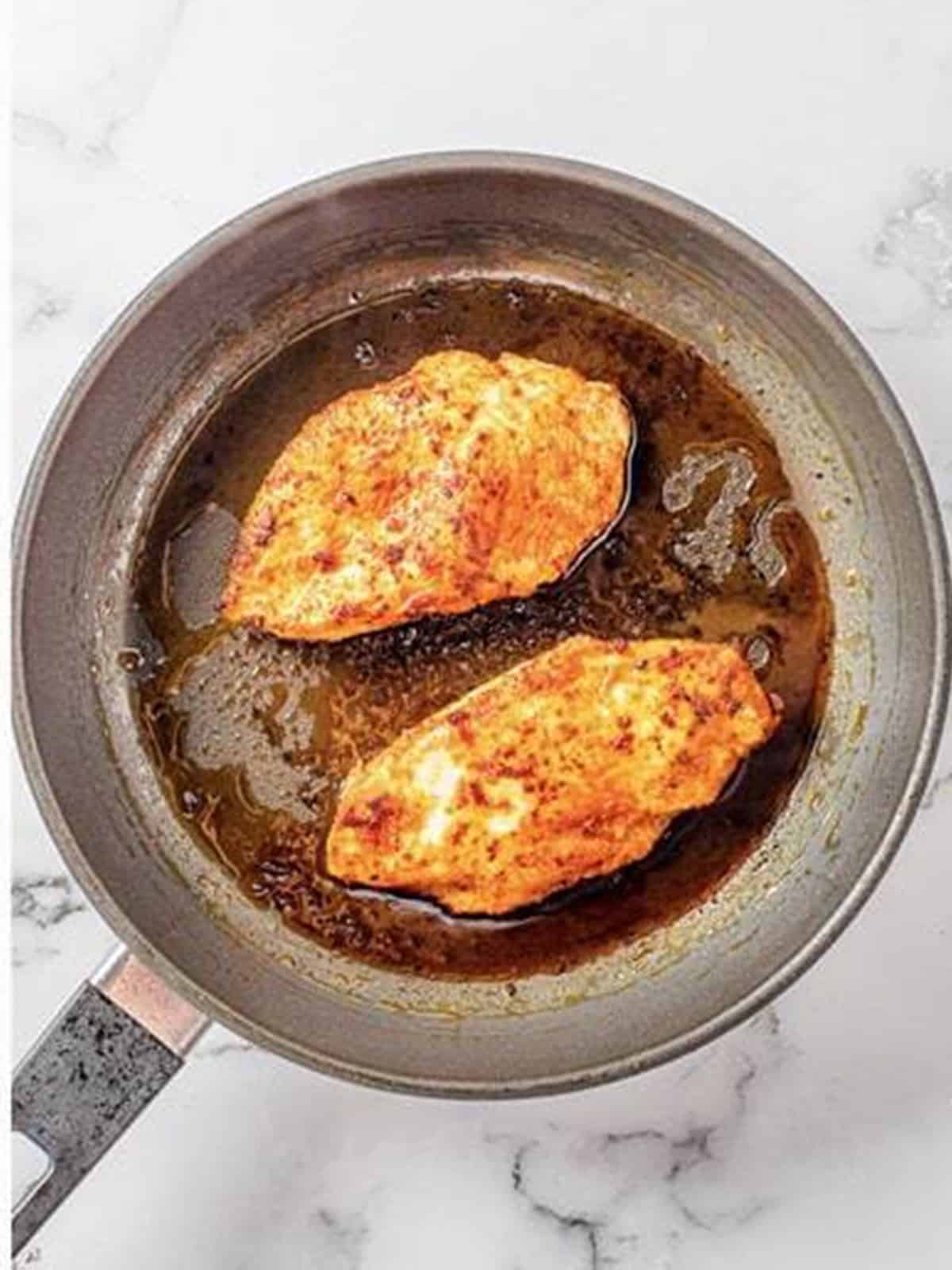 Seasoned chicken breasts searing golden brown in a skillet.
