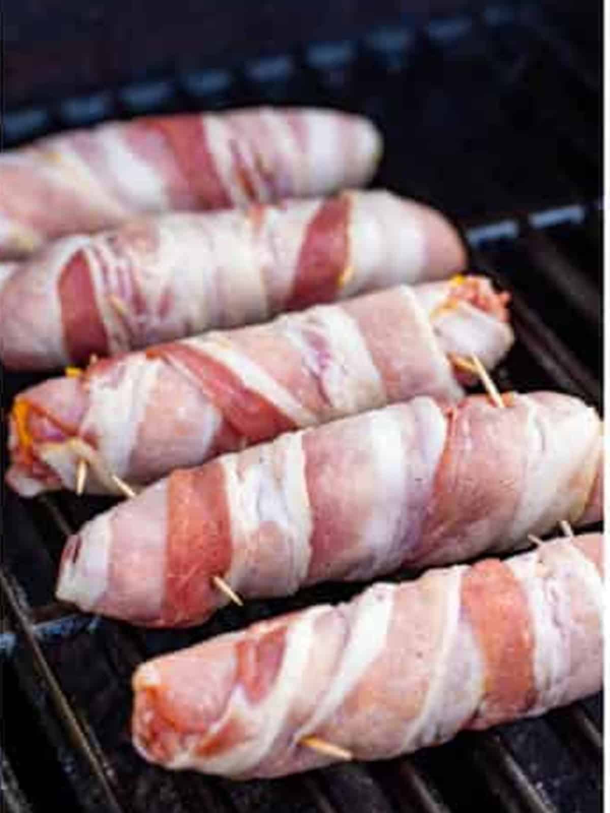 Bacon wrapped brats grilling on the grates.