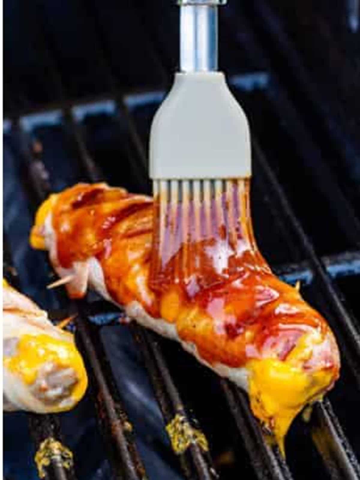 A bacon wrapped brat being basted with BBQ sauce on the grill.