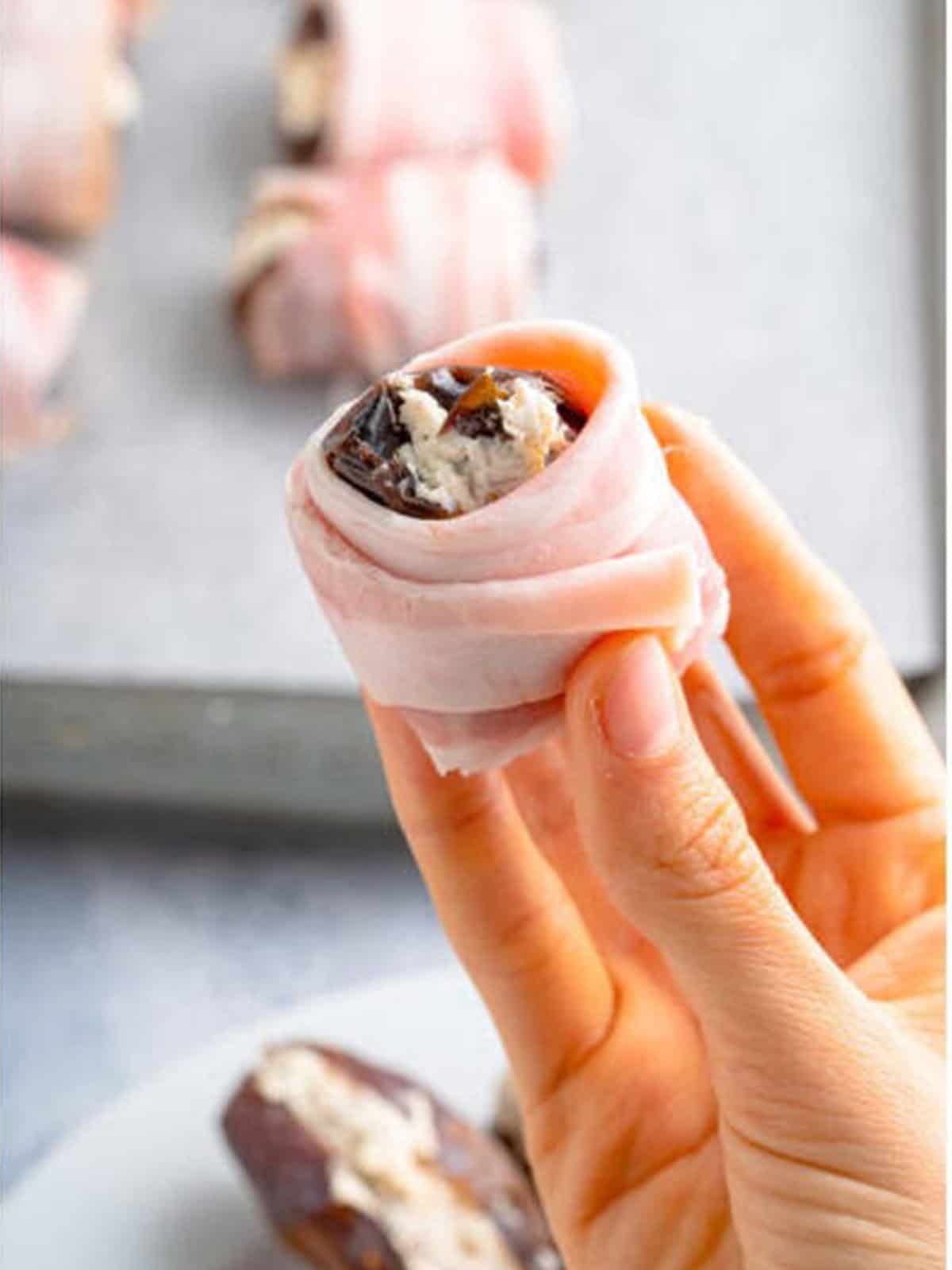 A stuffed date being wrapped in a slice of bacon and secured with a toothpick.