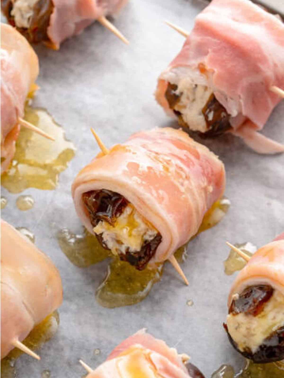 Bacon wrapped dates arranged on a parchment lined sheet tray and brushed with honey butter.
