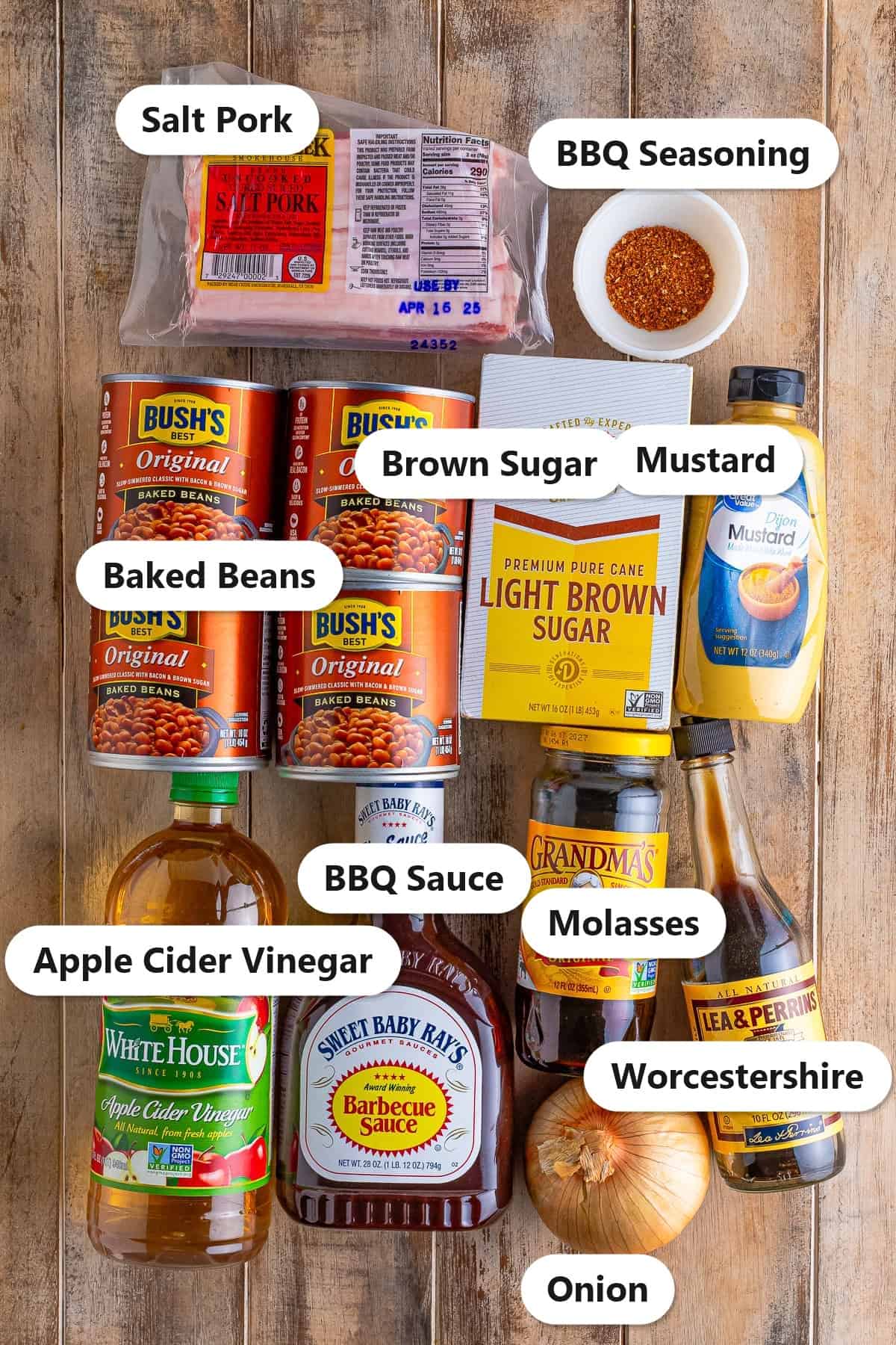 Labeled ingredients to make baked beans recipe including salt pork, canned baked beans, BBQ sauce, brown sugar, molasses, mustard, onion, and seasonings.