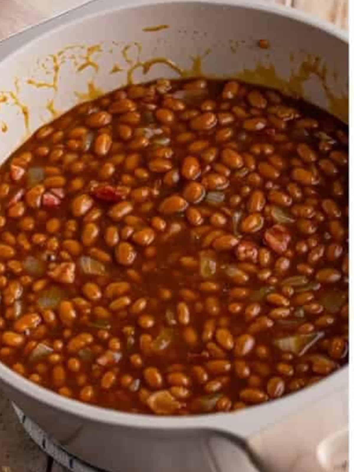 Baked beans stirred together with salt pork, onion, and sauce in a Dutch oven.