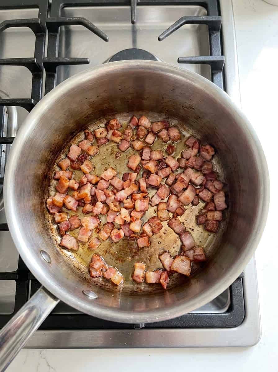 Diced bacon crisping in a stainless steel saucepan to start stove top baked beans.