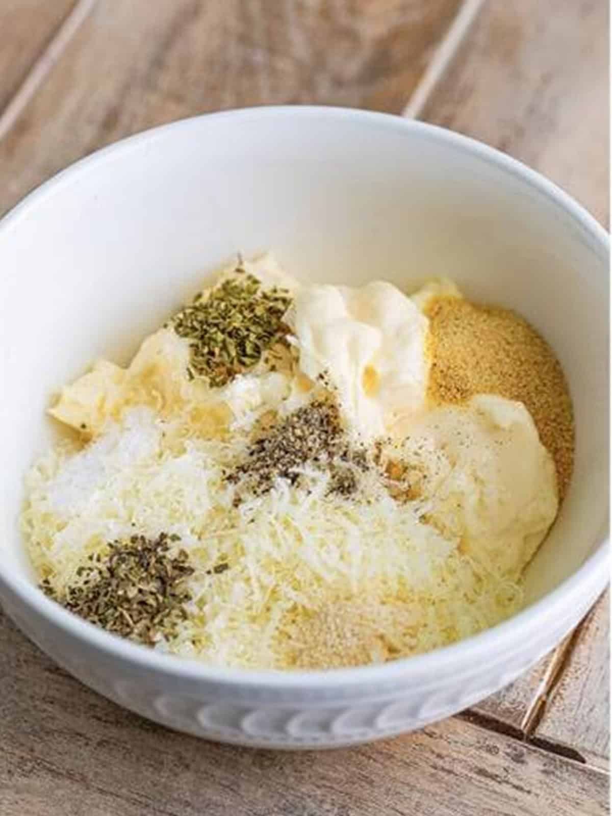 Parmesan, mayonnaise, and seasonings in a mixing bowl for baked chicken tenders coating.