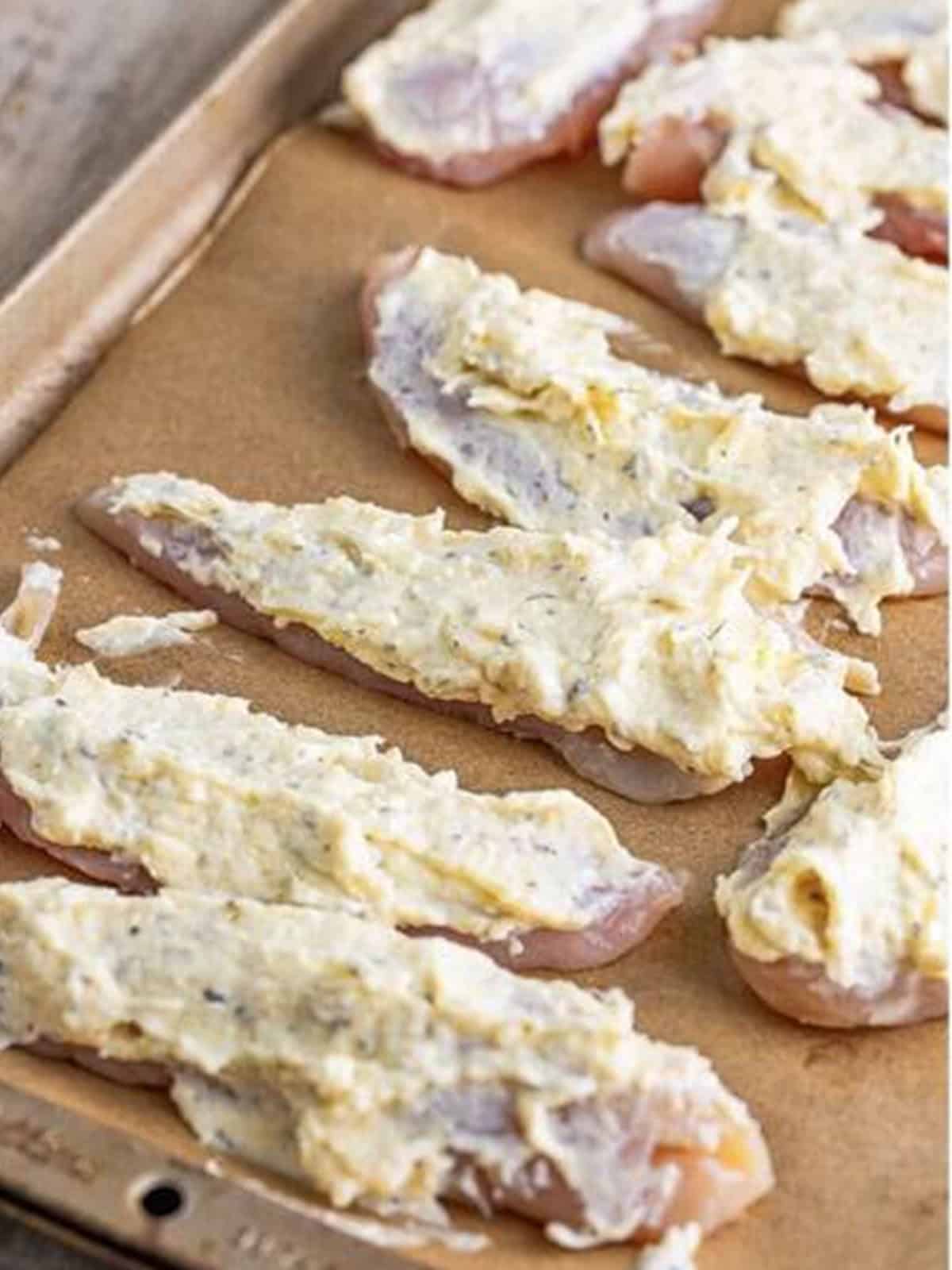 Spreading the parmesan mayonnaise coating over each chicken tender.
