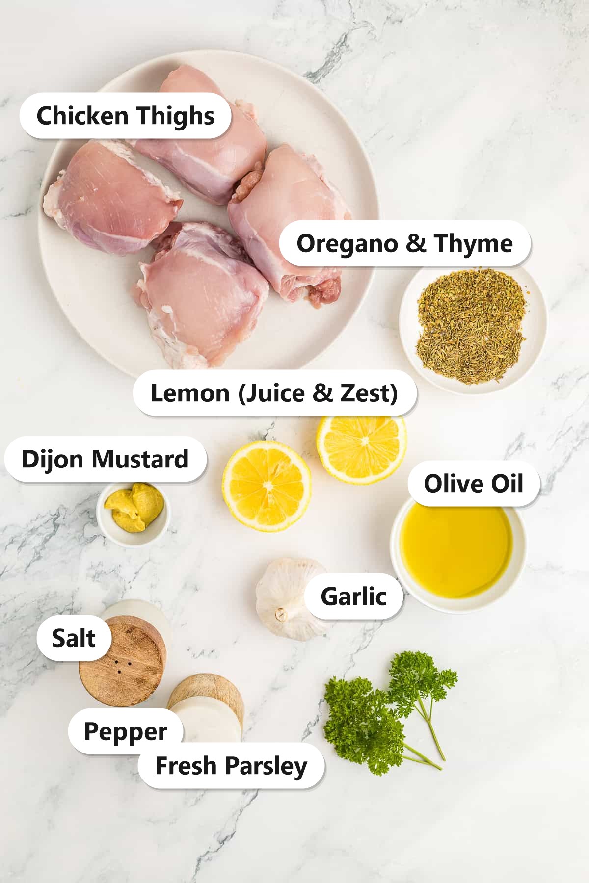 Labeled ingredients for baked chicken thighs: chicken thighs, lemon, garlic, olive oil, Dijon mustard, oregano, thyme, salt, pepper, and fresh parsley.