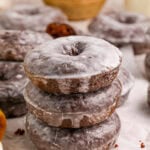 A stack of glazed baked chocolate donuts on parchment paper.