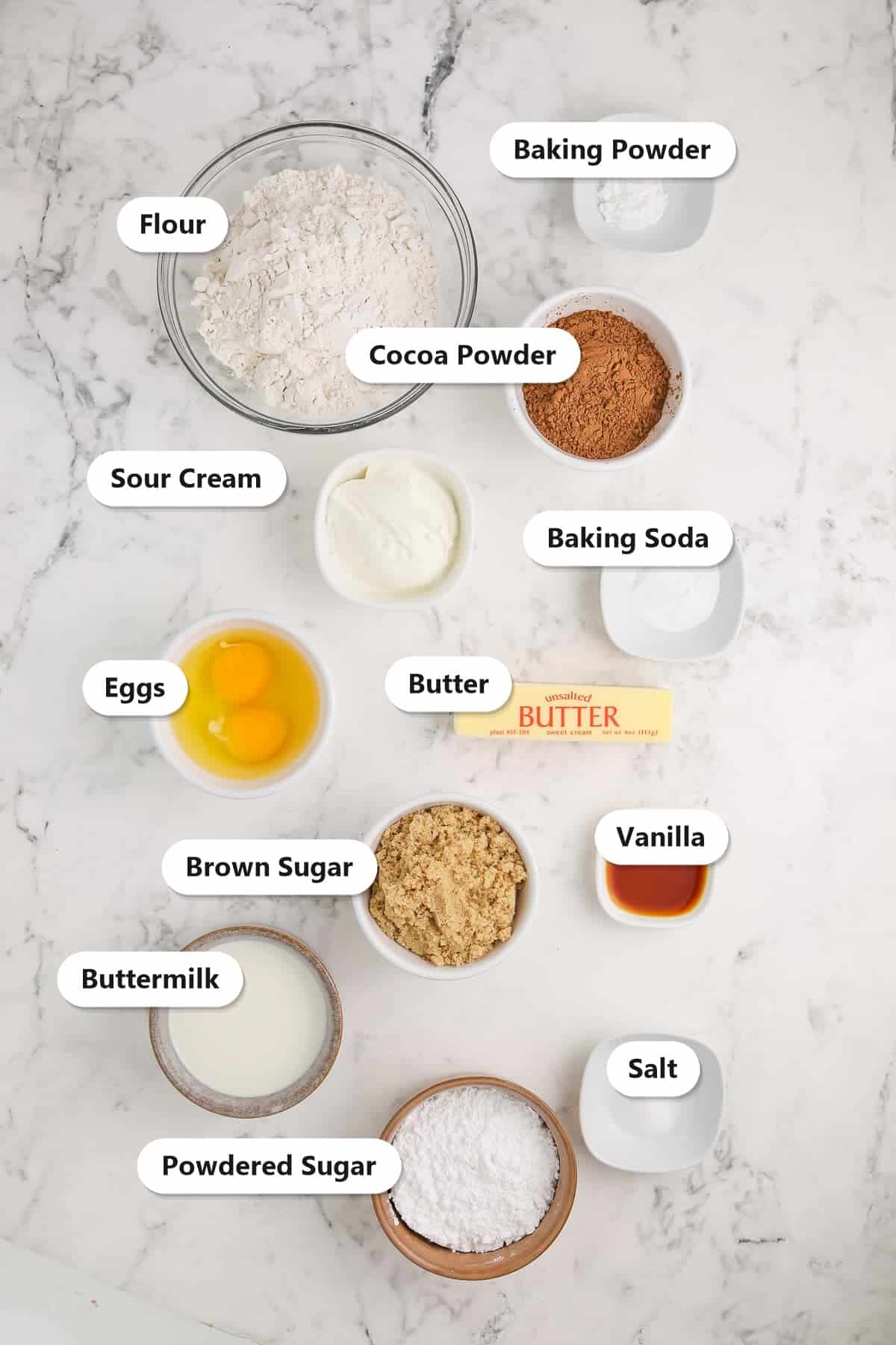 Labeled ingredients for baked chocolate donuts including flour, cocoa powder, butter, brown sugar, eggs, sour cream, buttermilk, and powdered sugar.