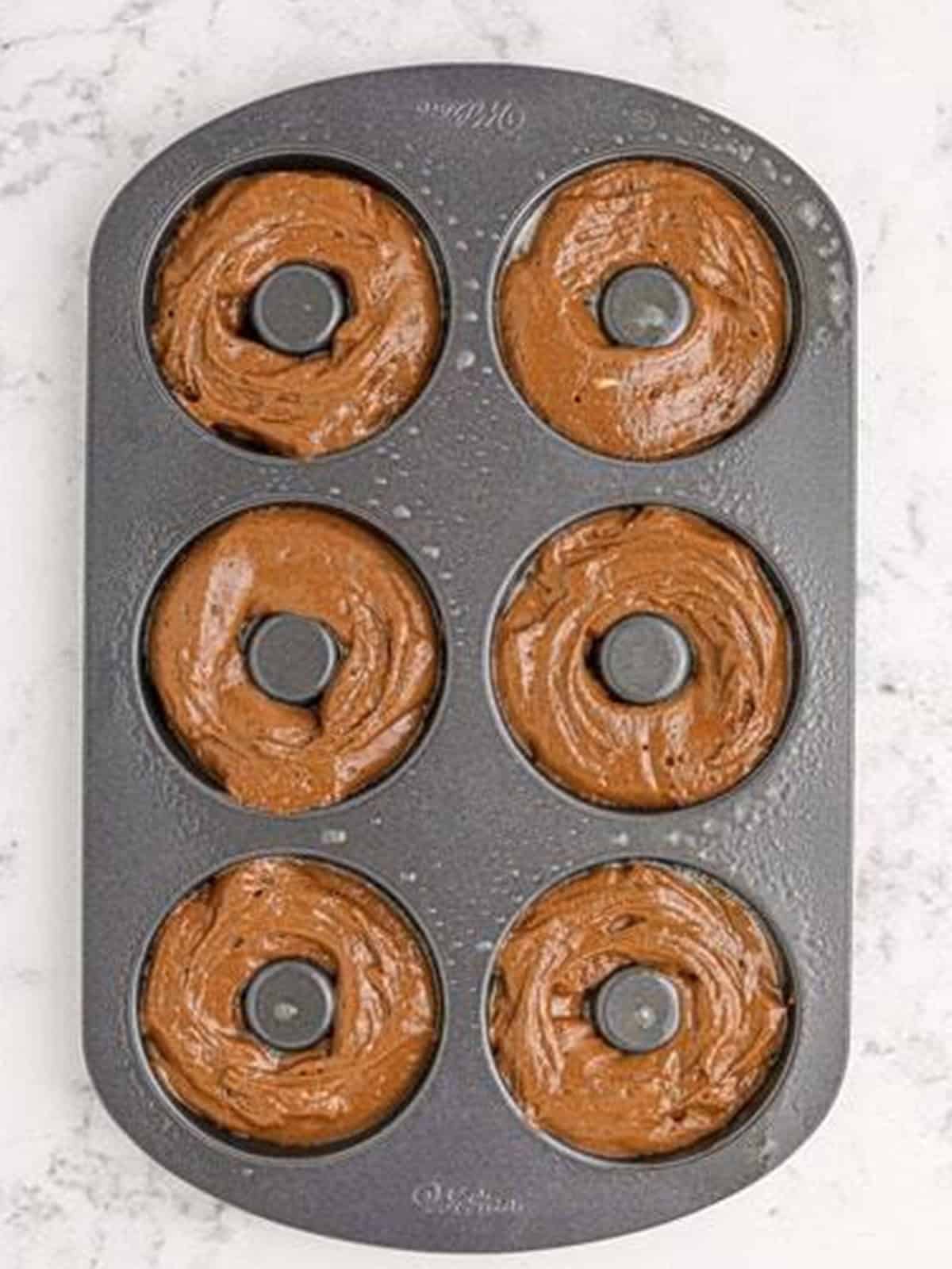 Chocolate donut batter piped into a donut baking pan.