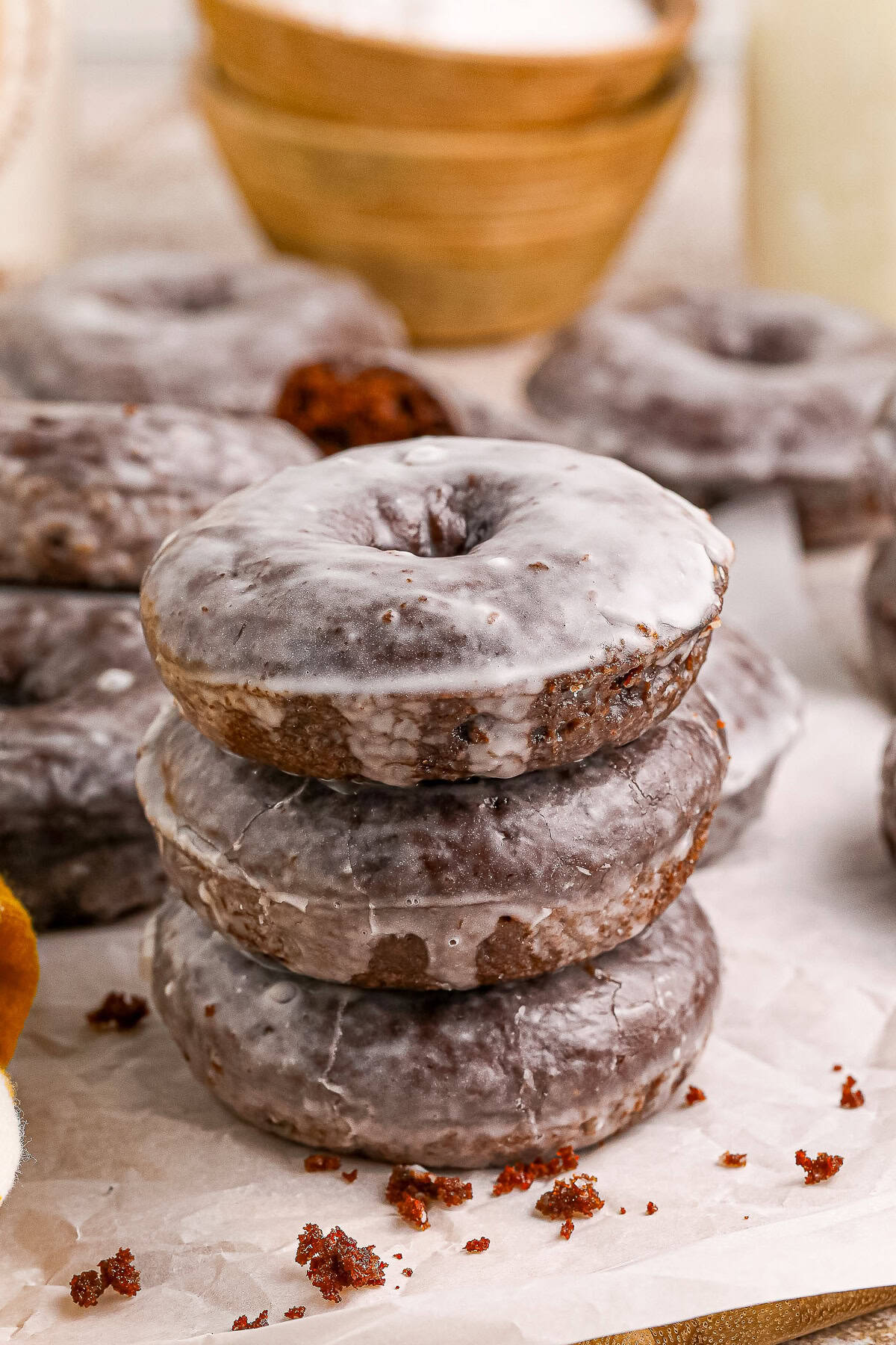 A stack of glazed baked chocolate donuts on parchment paper.
