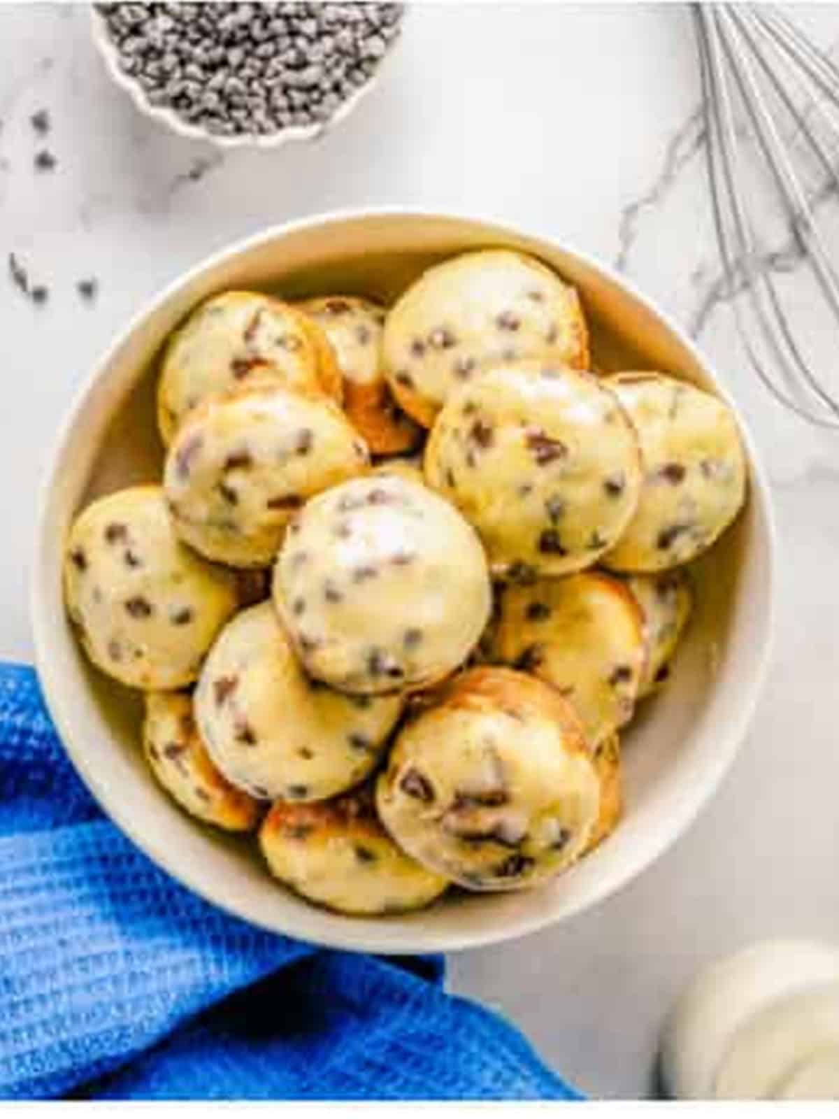 Glazed chocolate chip donut holes piled in a white bowl.