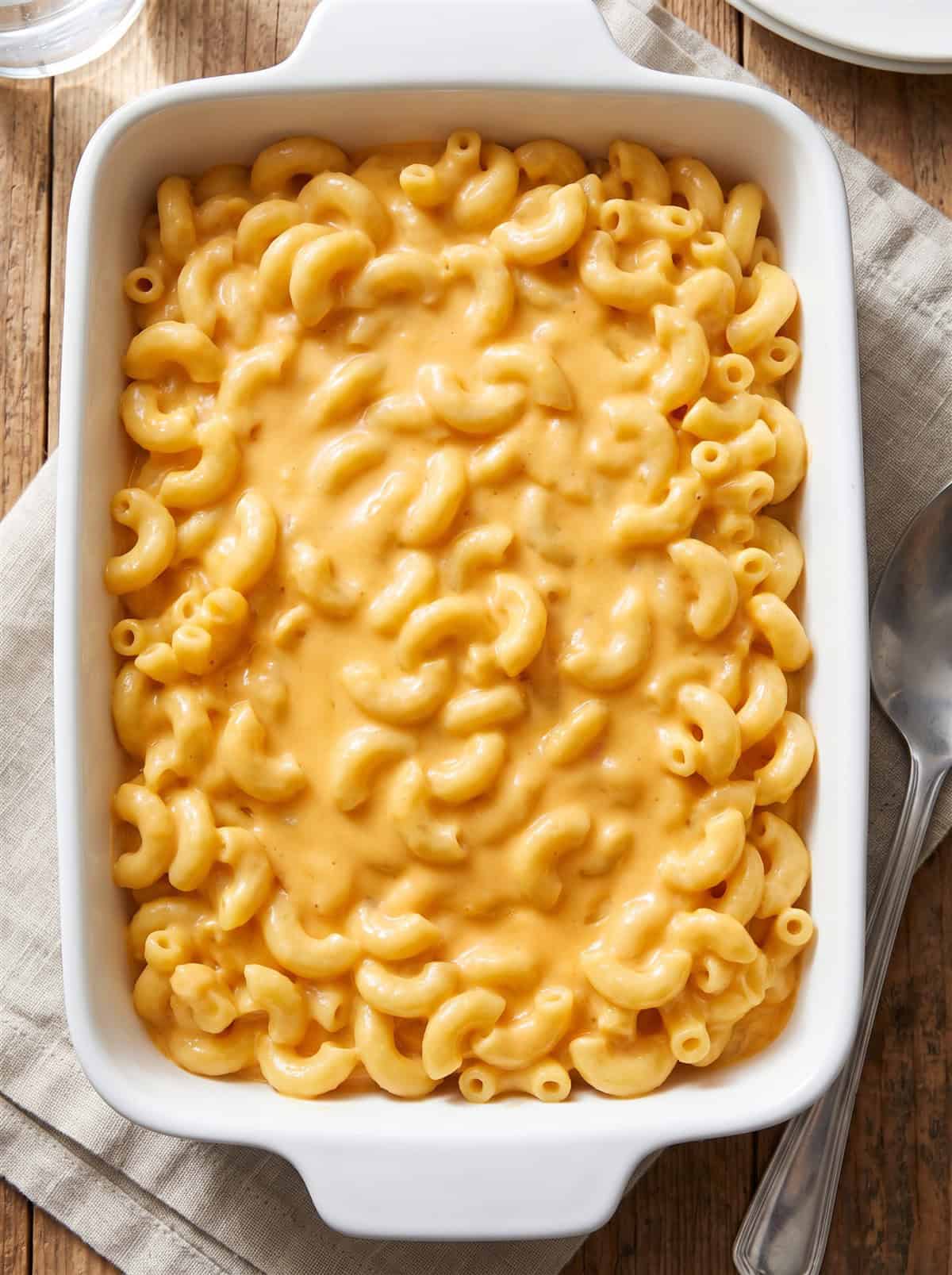 Cooked elbow macaroni folded into creamy cheese sauce in a white baking dish.