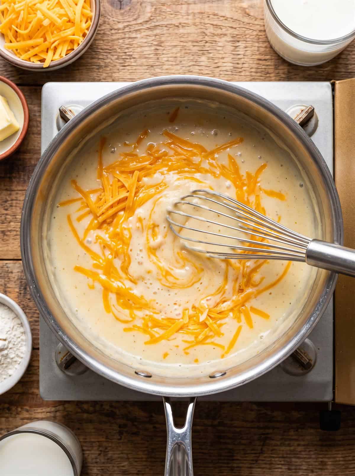 Creamy cheddar cheese sauce being whisked in a saucepan.