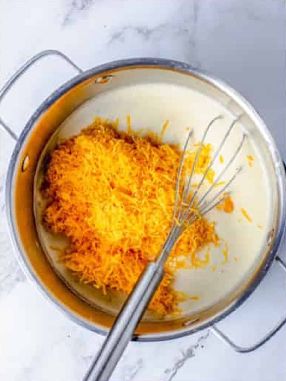 Whisking shredded sharp cheddar into the milk sauce until smooth and melted.