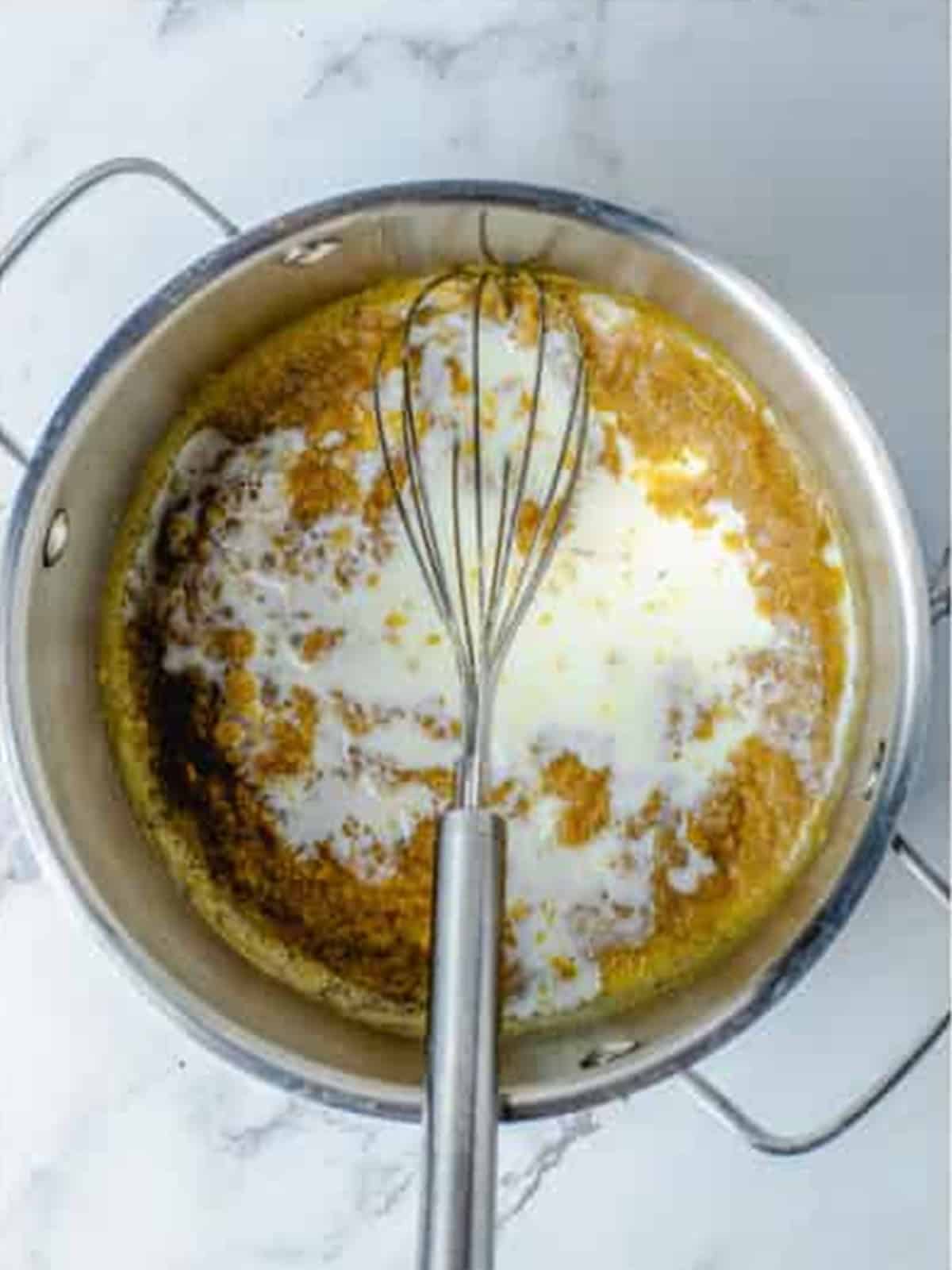 Streaming whole milk into the roux to build the cheese sauce for Baked Mac and Cheese.