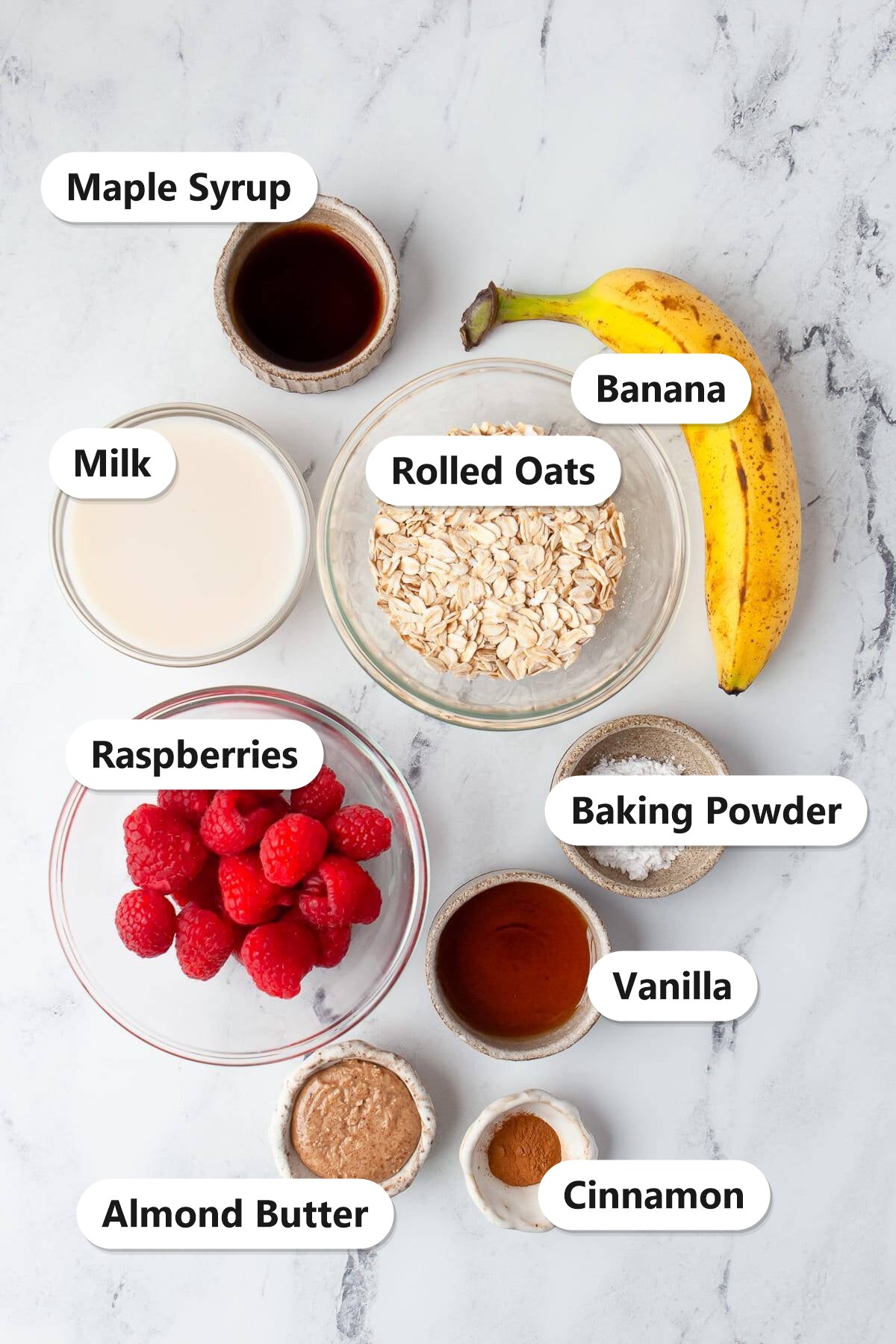 Baked oats ingredients labeled including banana, rolled oats, milk, maple syrup, almond butter, raspberries, and cinnamon.