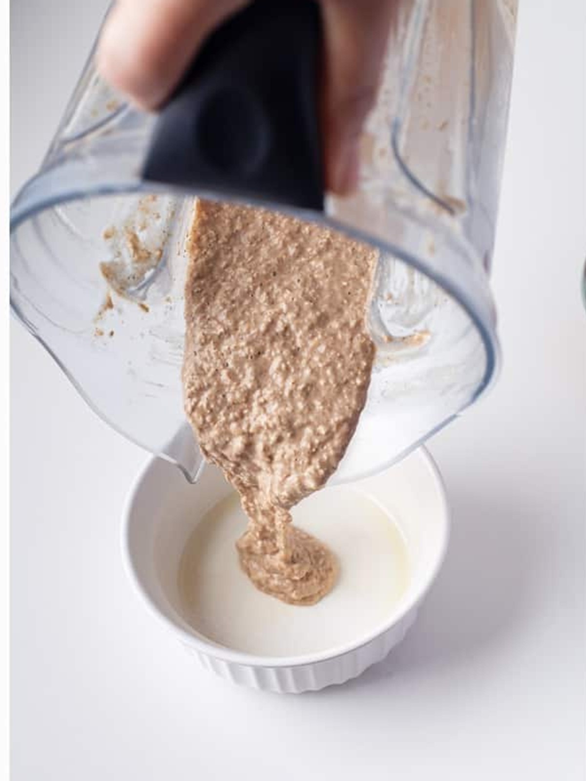 Pouring the blended baked oats batter from a blender into a dish.