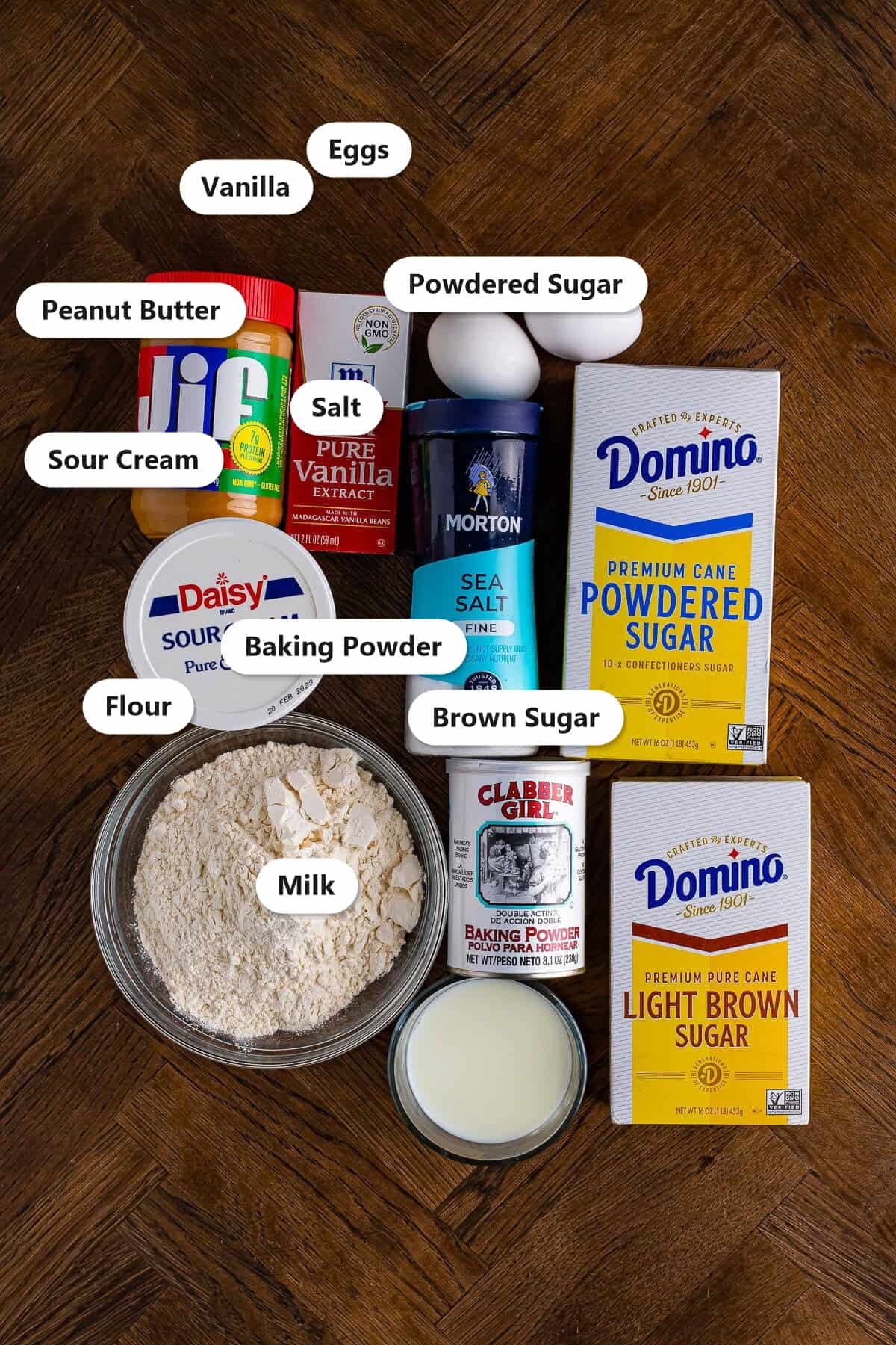 Labeled ingredients for baked peanut butter donuts including peanut butter, vanilla, eggs, powdered sugar, sour cream, salt, flour, baking powder, brown sugar, and milk.