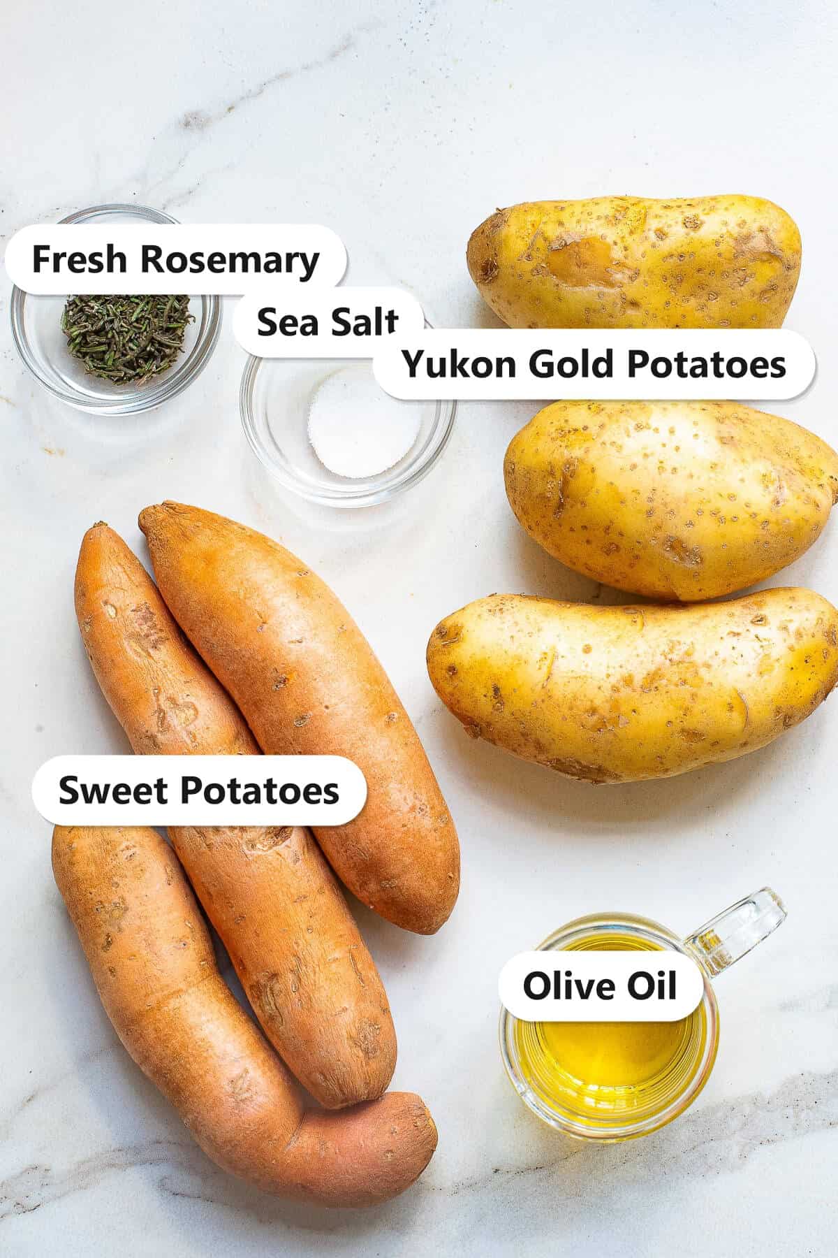 Baked potato chips ingredients including Yukon gold potatoes, sweet potatoes, olive oil, sea salt, and fresh rosemary labeled on a marble surface.