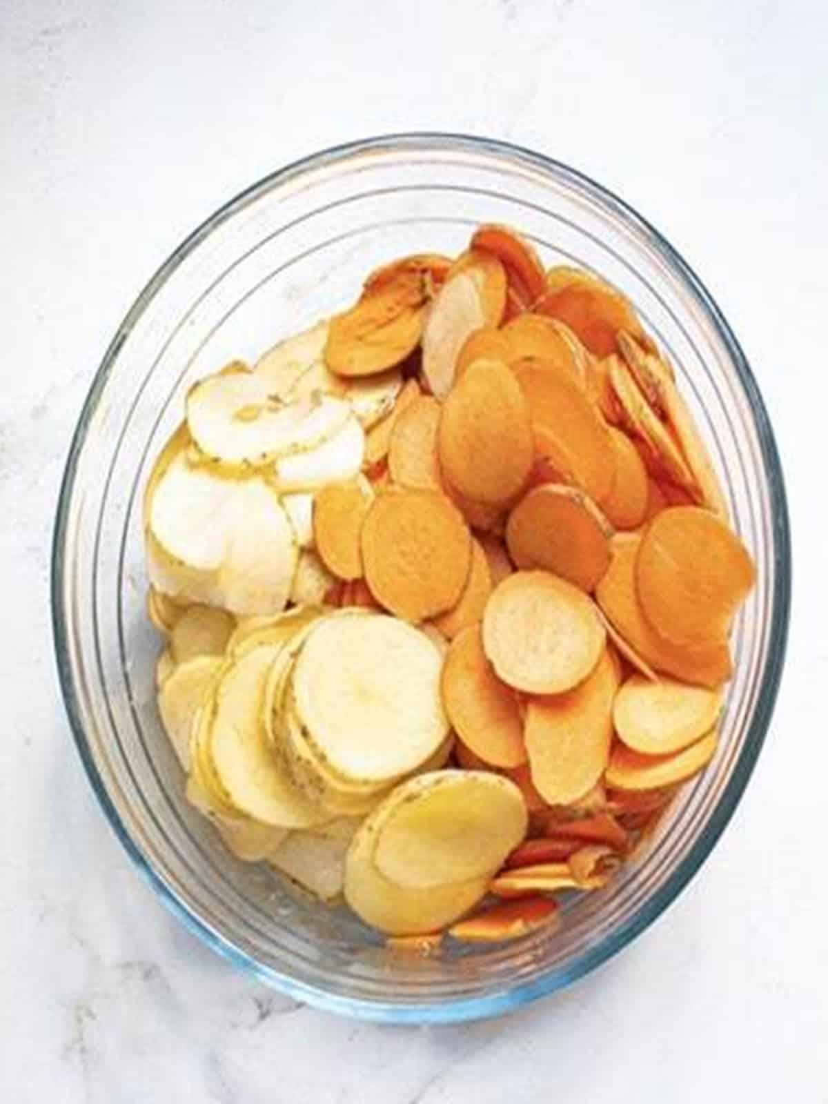 Thinly sliced Yukon gold and sweet potatoes in a glass bowl for baked potato chips.