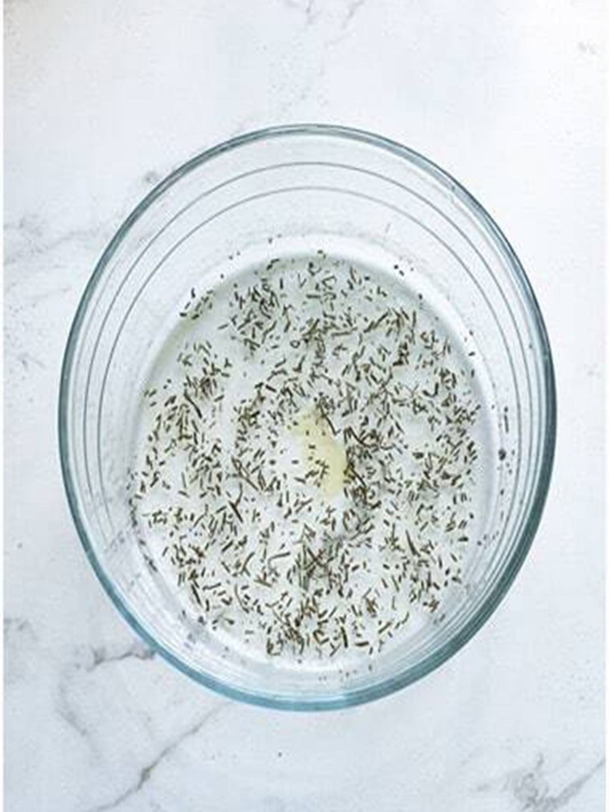 Olive oil, sea salt, and rosemary mixed together in a bowl for baked potato chips.
