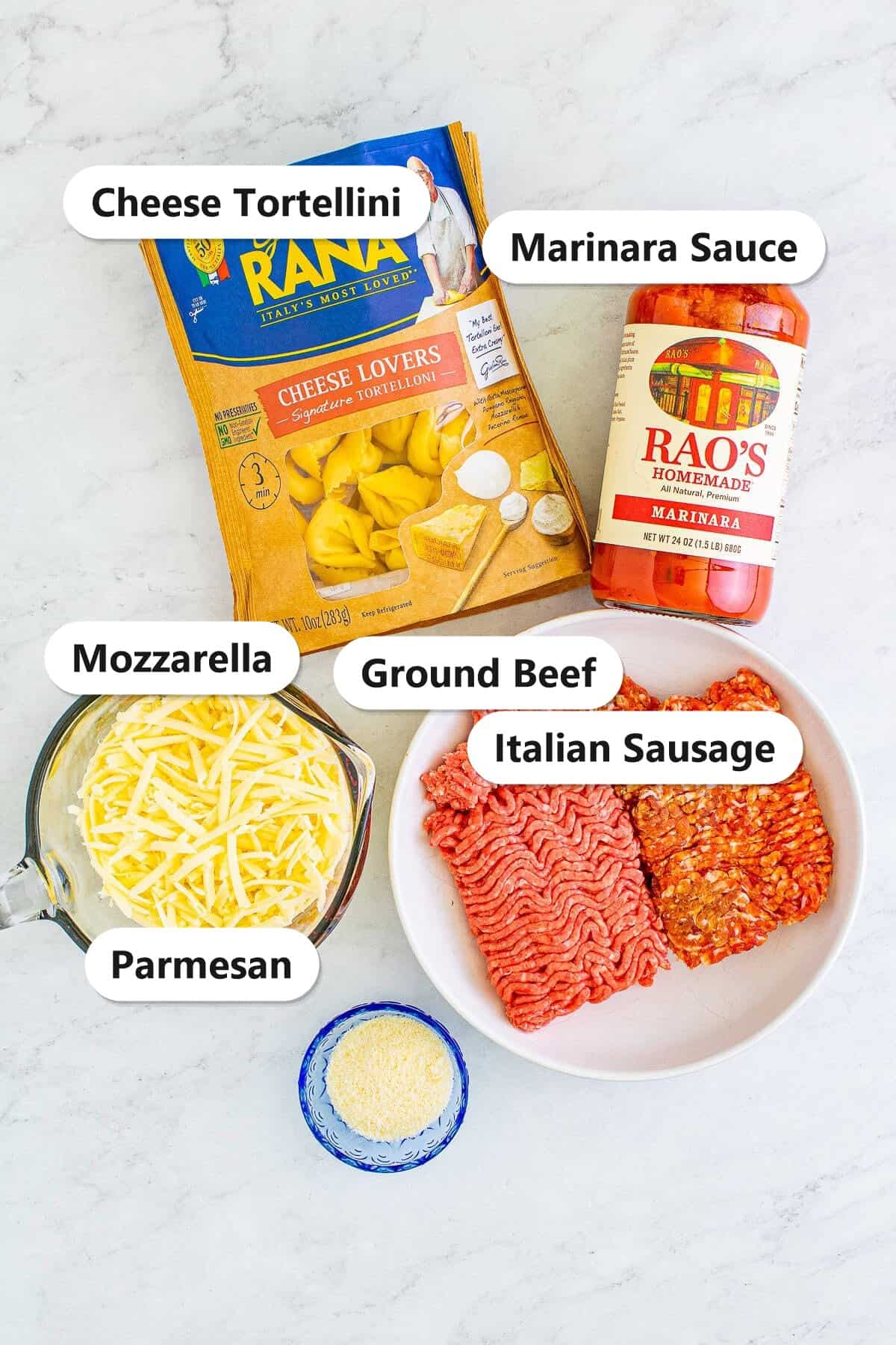 Labeled ingredients to make baked tortellini with meat sauce including cheese tortellini, marinara, ground beef, Italian sausage, mozzarella, and parmesan.