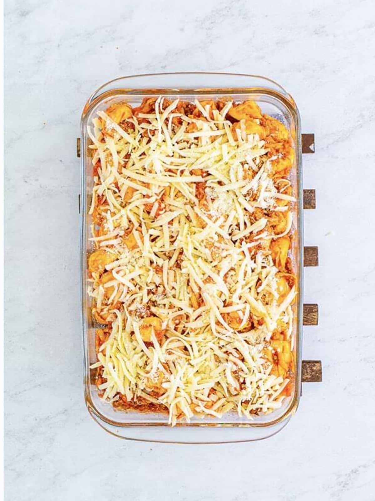 Tortellini and meat sauce in a baking dish topped with shredded mozzarella before baking.