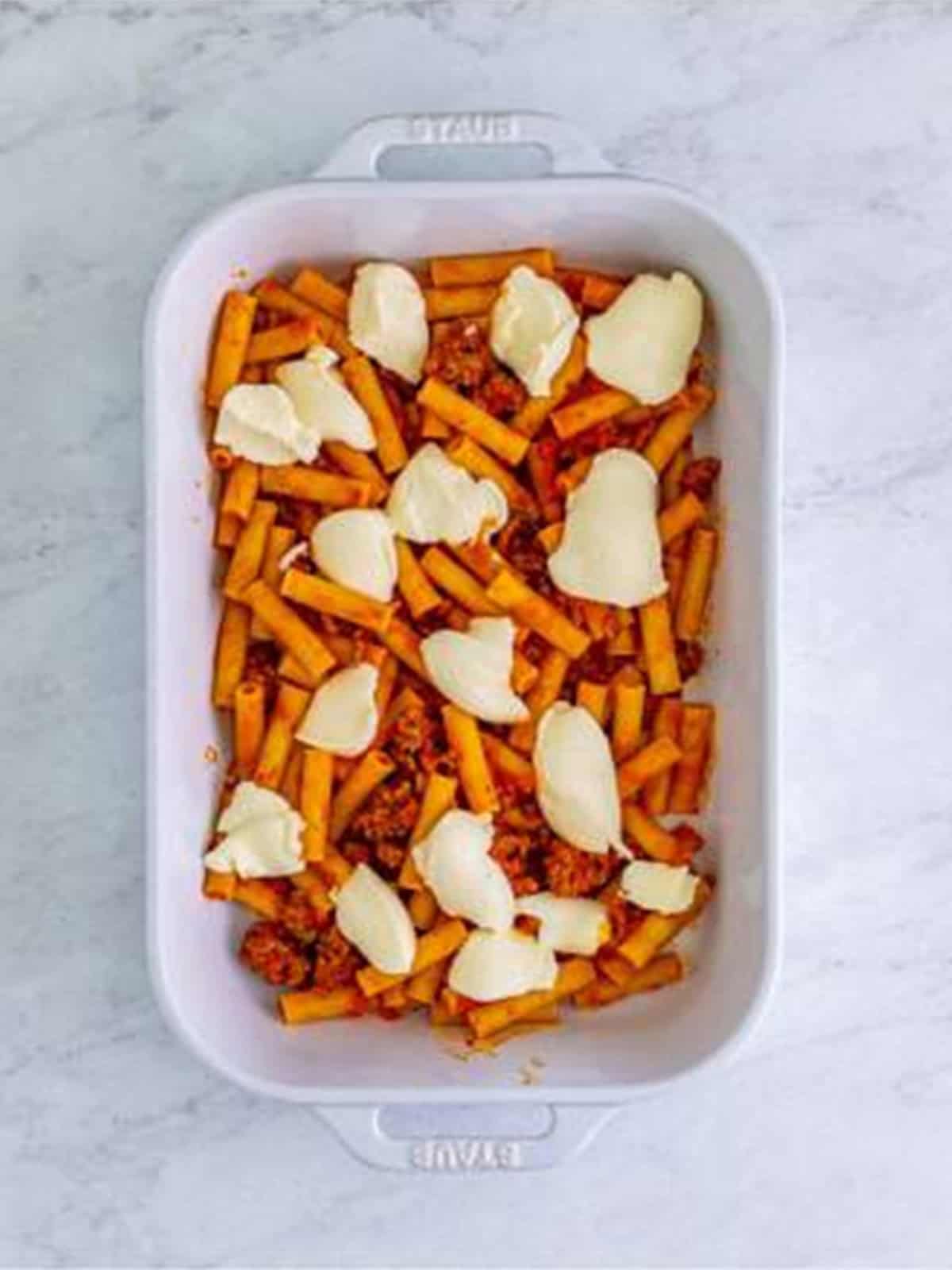 Dolloping ricotta cheese over a layer of ziti in a baking dish