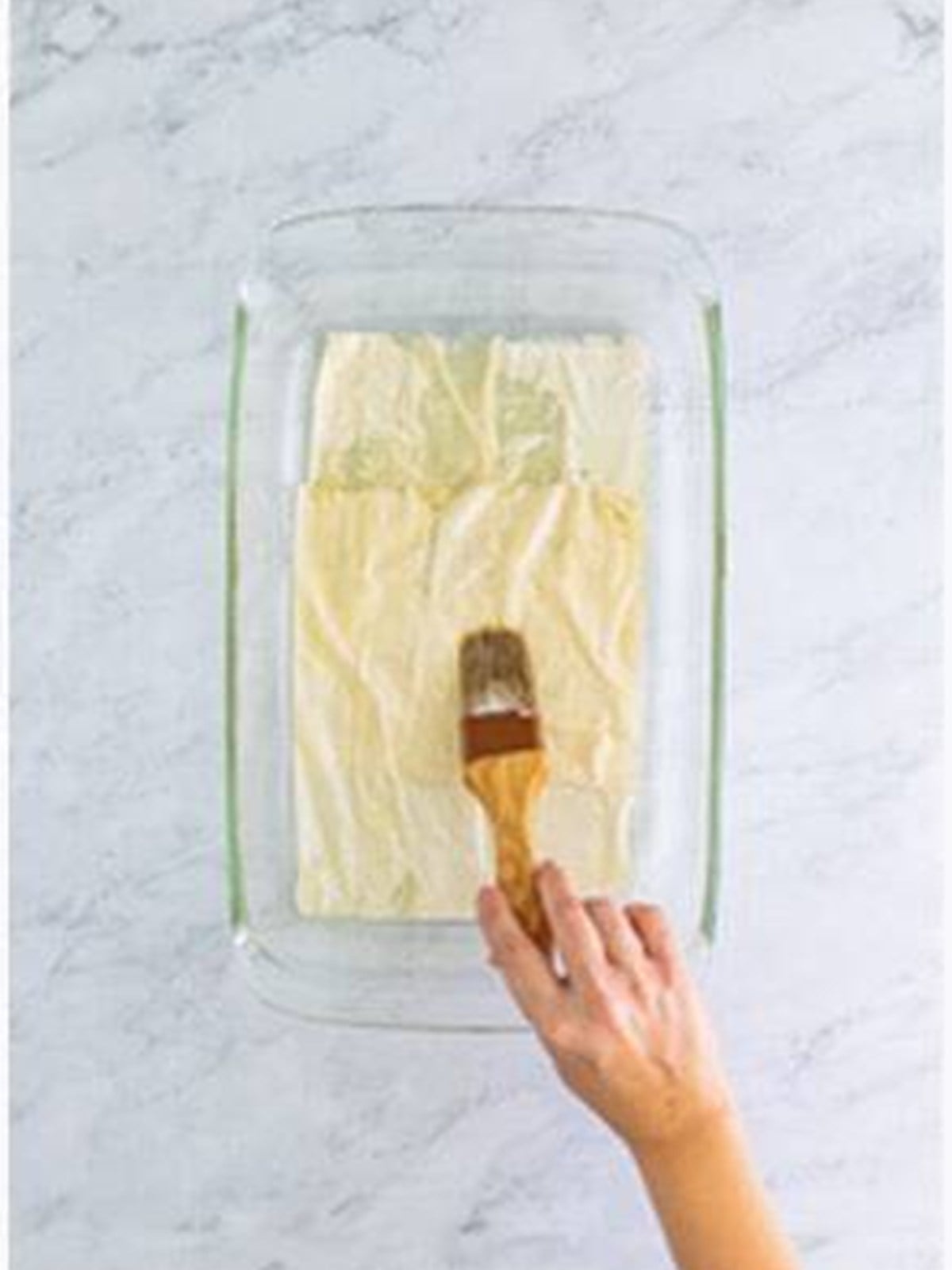 Brushing melted butter over layers of phyllo dough in a baking dish