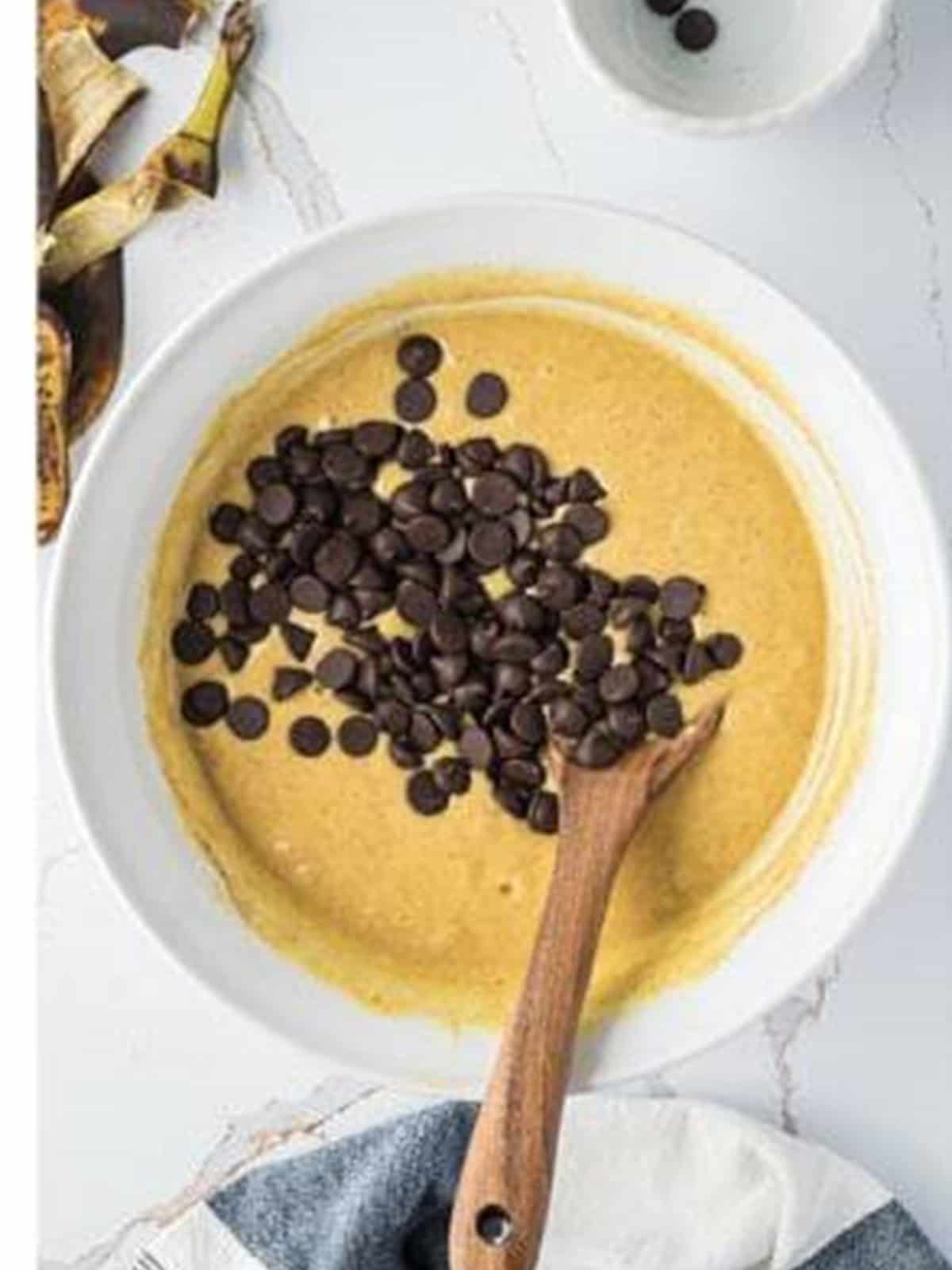 Chocolate chips folded into the banana bundt cake batter with a wooden spoon.