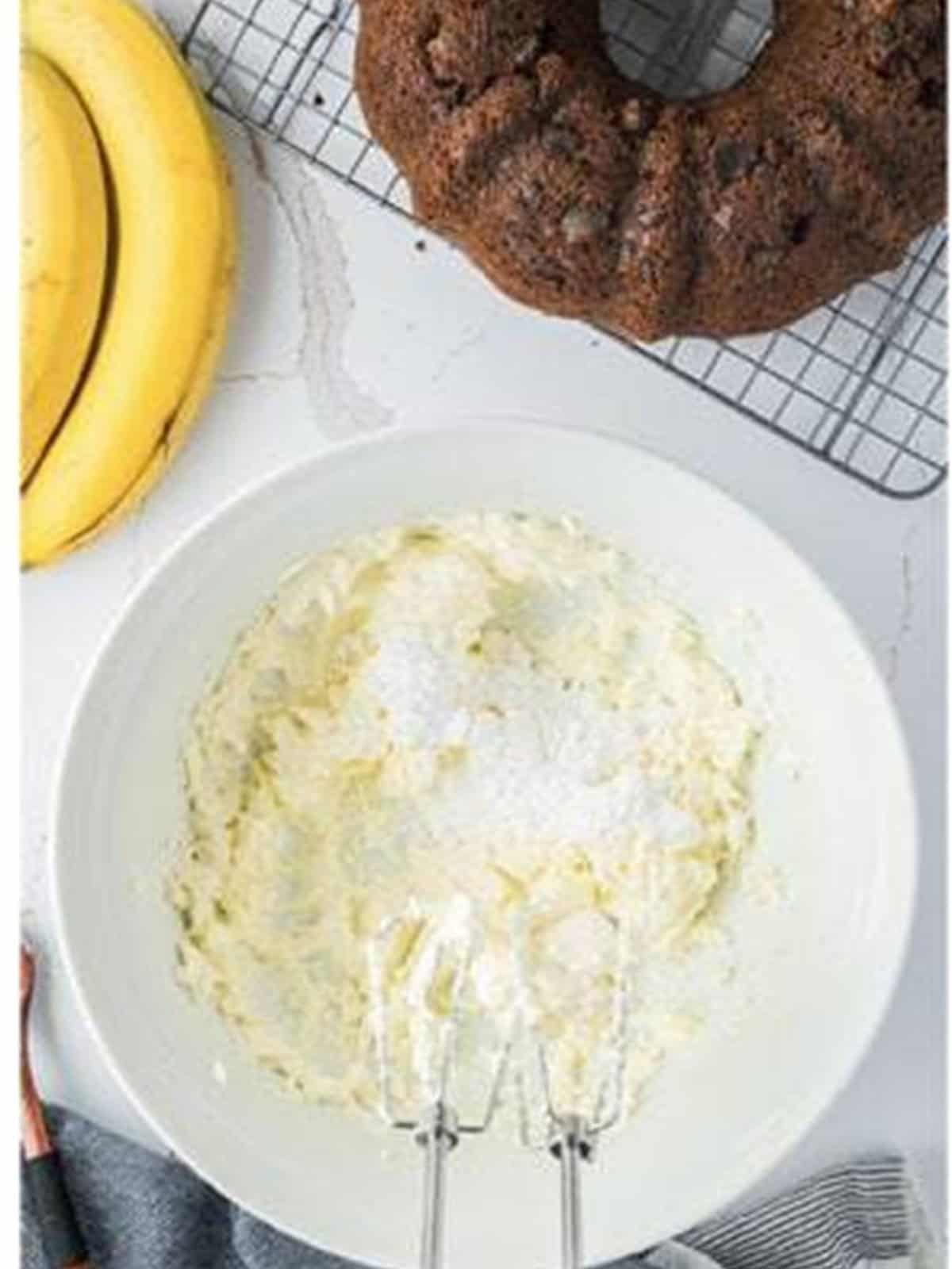 Cream cheese, butter, and powdered sugar blending into frosting with a hand mixer.